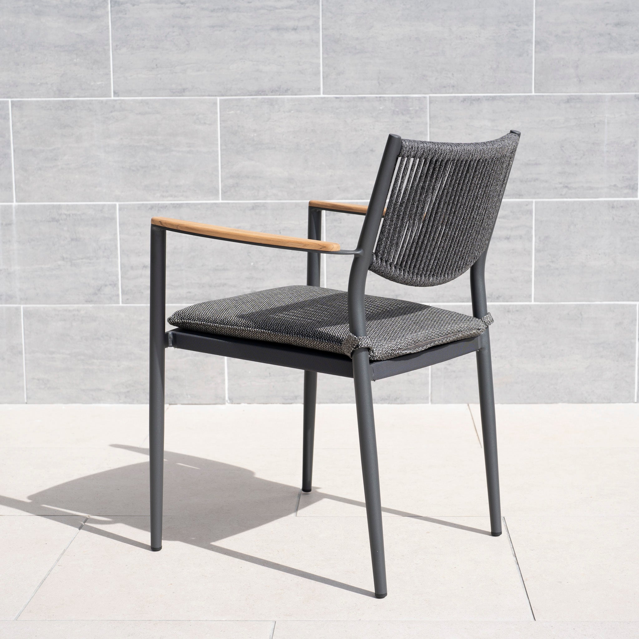 The Tellaro Rope Dining Chair in Grey (6pcs) features a woven seat and back, metal frame, and wooden armrests—ideal for outdoor dining on a light tile floor.