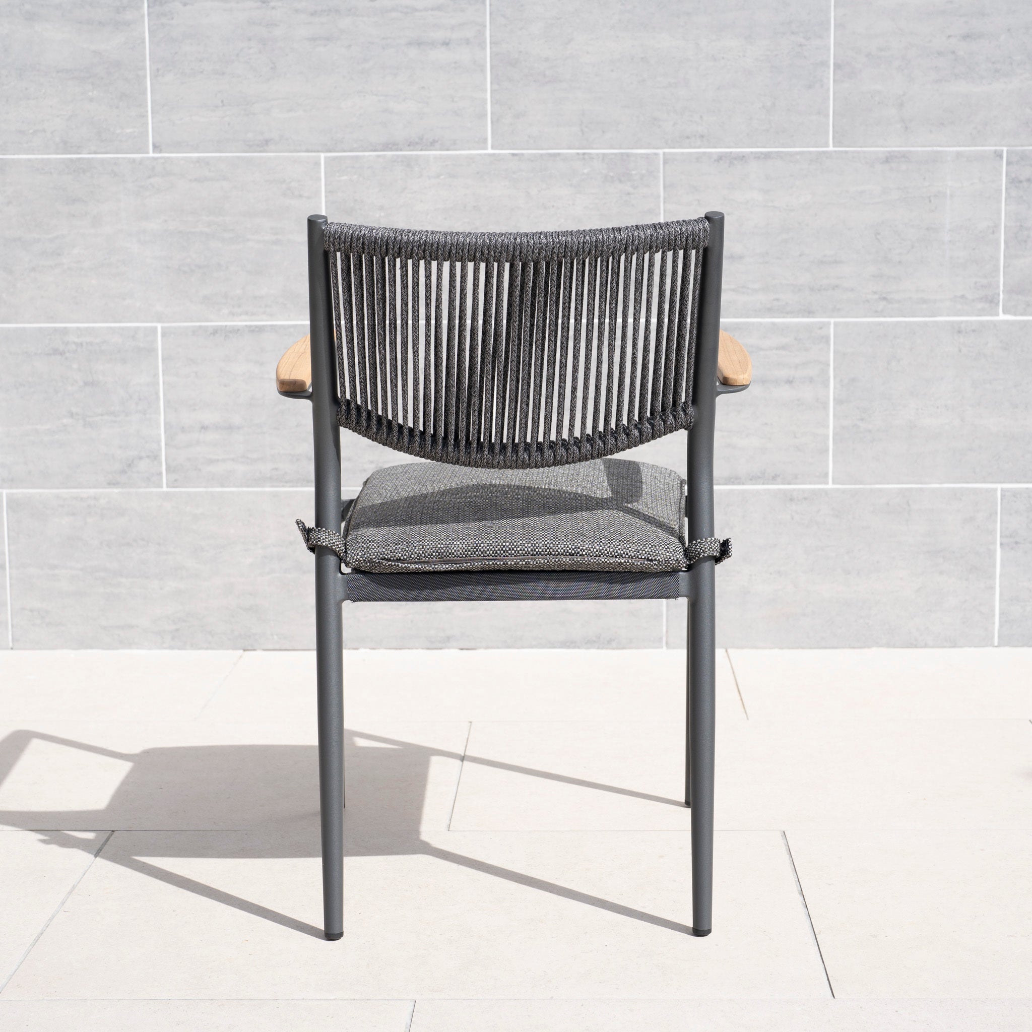 The Tellaro Rope Dining Chair in Grey (6pcs) features a woven backrest, metal frame, and weather-resistant cushion, shown here on a light tiled patio.