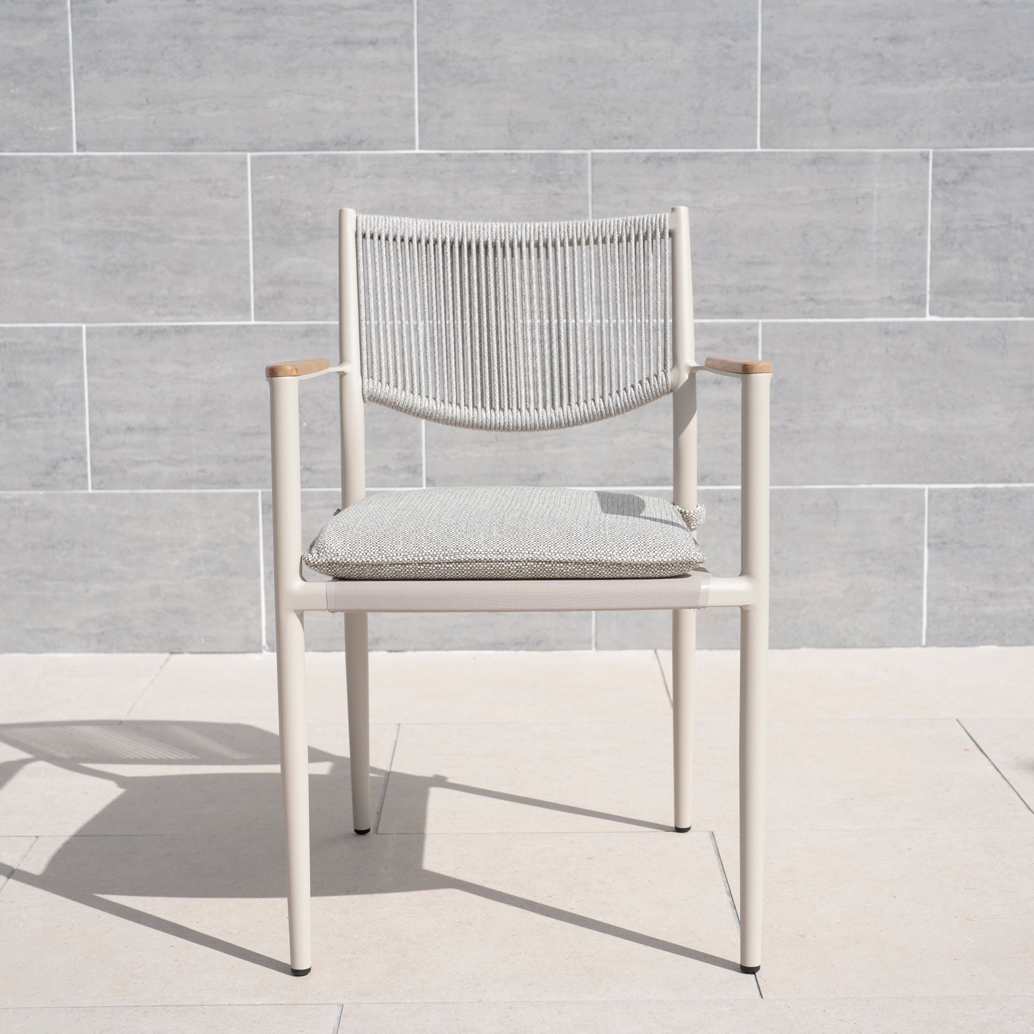 The Tellaro Rope Dining Chair in Latte (6pcs) features a hand-woven rope backrest and cushion, displayed on a light stone floor against a tiled wall.