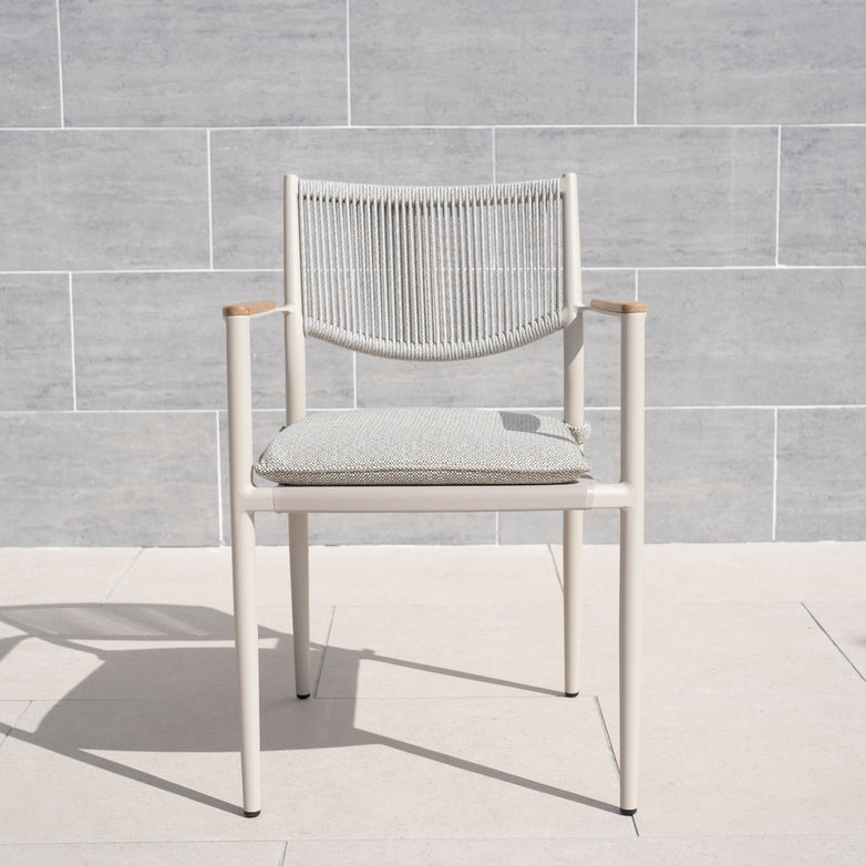 The Tellaro Rope Dining Chair in Latte (6pcs) features a hand-woven rope backrest and cushion, displayed on a light stone floor against a tiled wall.