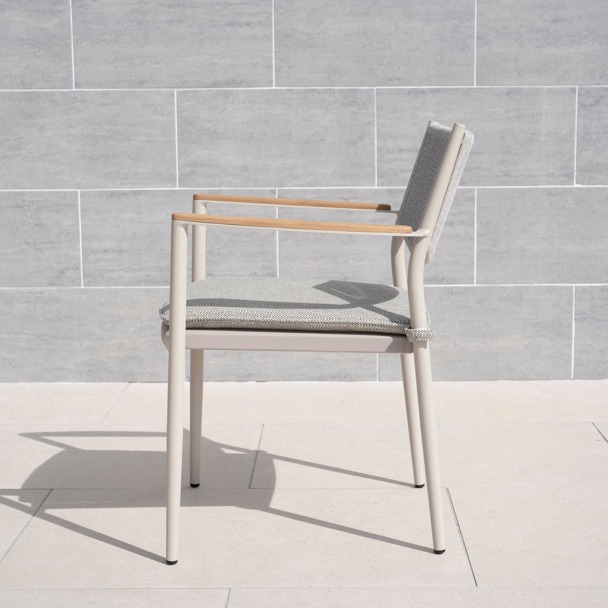 A set of Tellaro Rope Dining Chairs in Latte, featuring wooden armrests and a hand-woven rope backrest, is arranged on a light tile floor against a gray tiled wall.