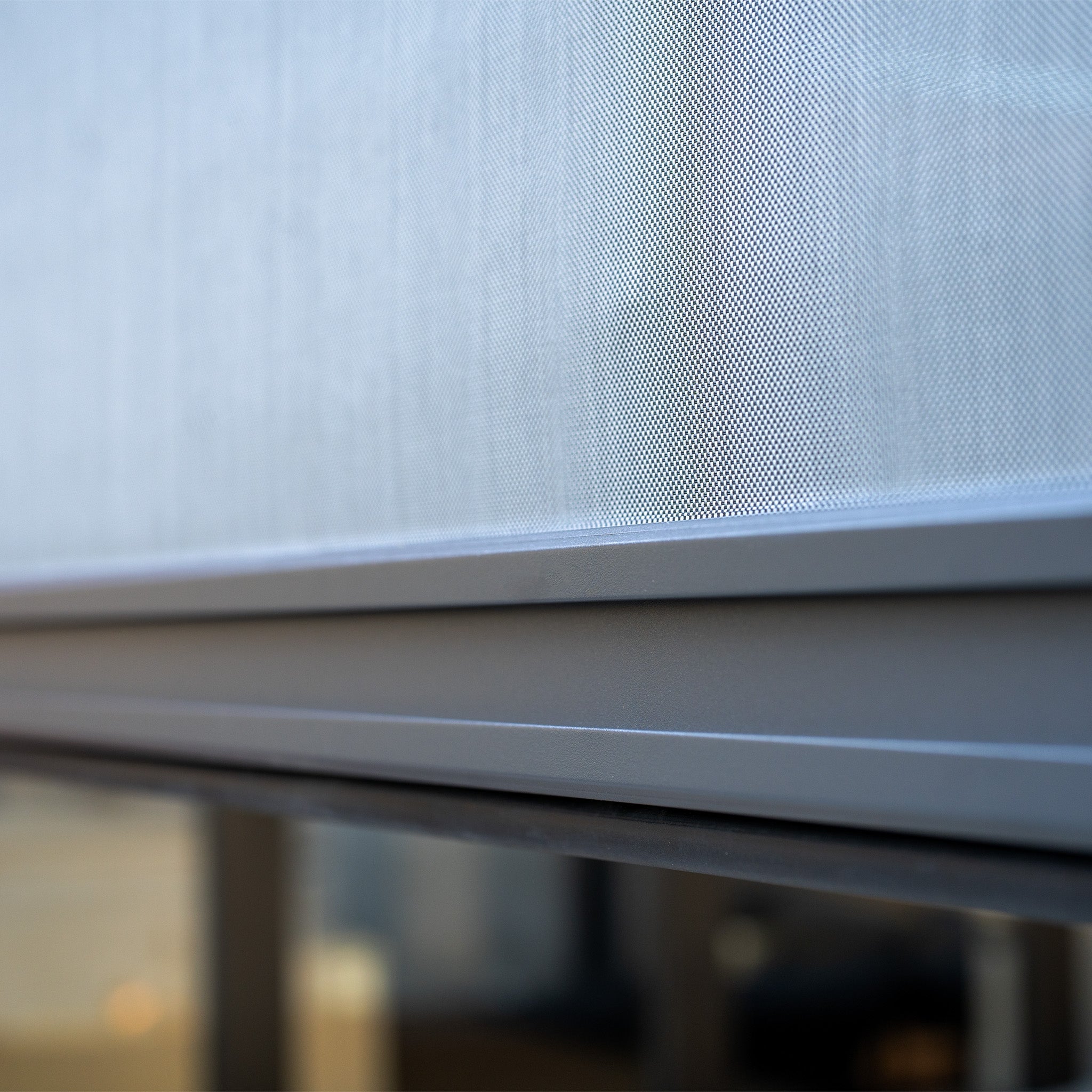 Close-up of a perforated metal panel with a blurred reflection behind it, reminiscent of the sleek design found in the PergoSTET Plus 3m x 4m Rectangular Pergola with 3 Drop Sides and LED Lighting in Grey.