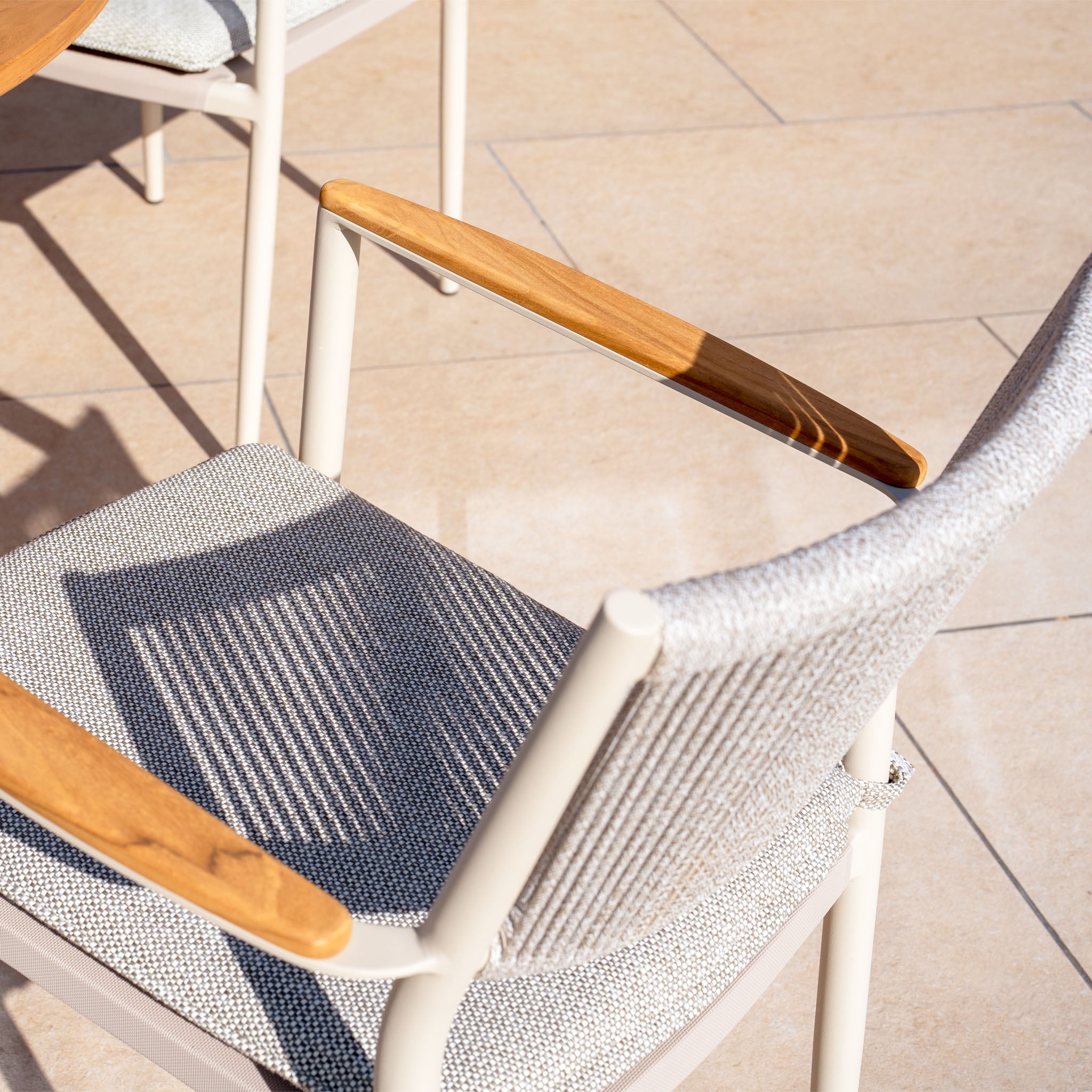 Tellaro Rope Dining Chair in Latte (set of 4) features wooden armrests and a light fabric seat, casting elegant shadows on tiled flooring.