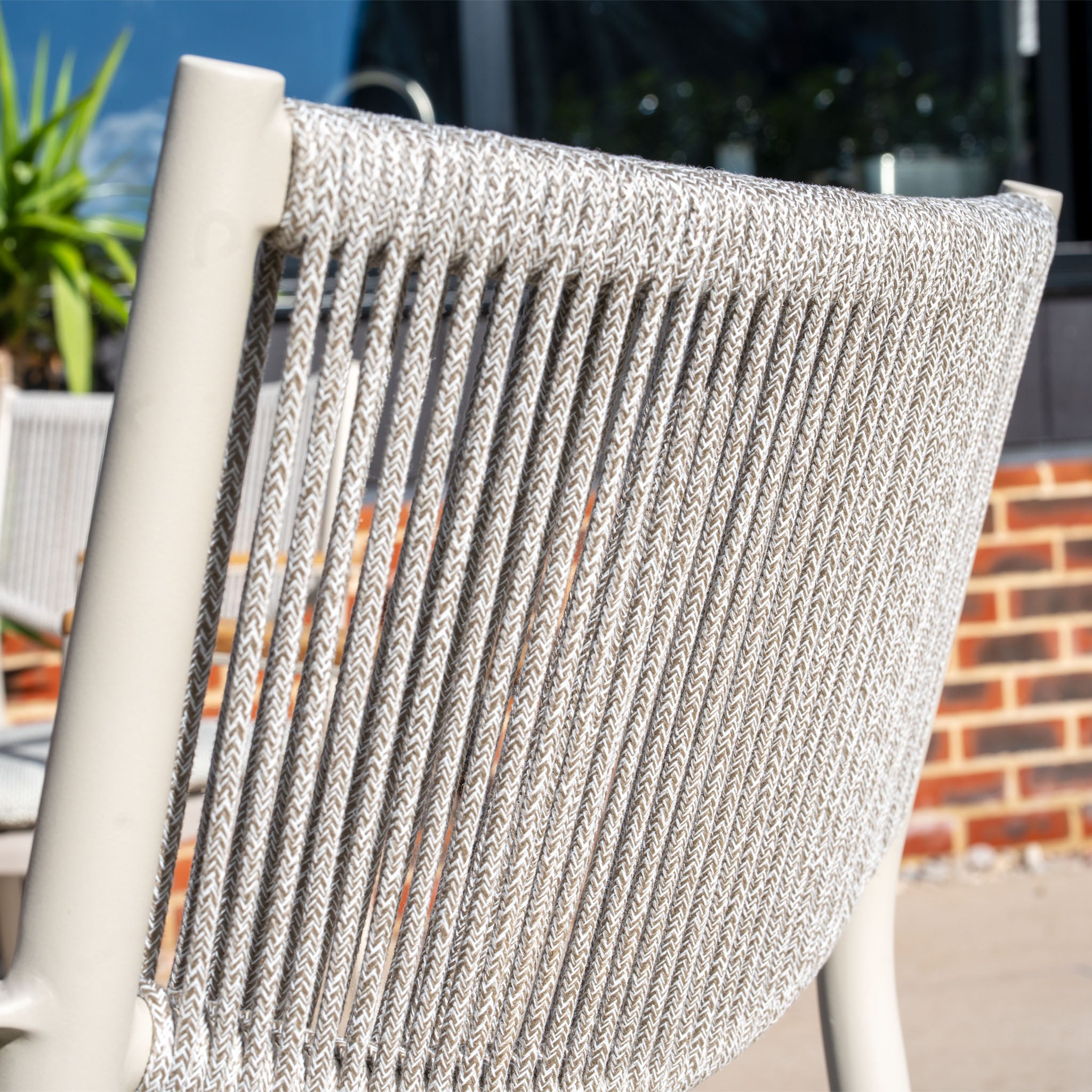 Close-up of the Tellaro Rope Dining Chair in Latte (set of 4), featuring a woven backrest with sunlight and a brick wall in the background.