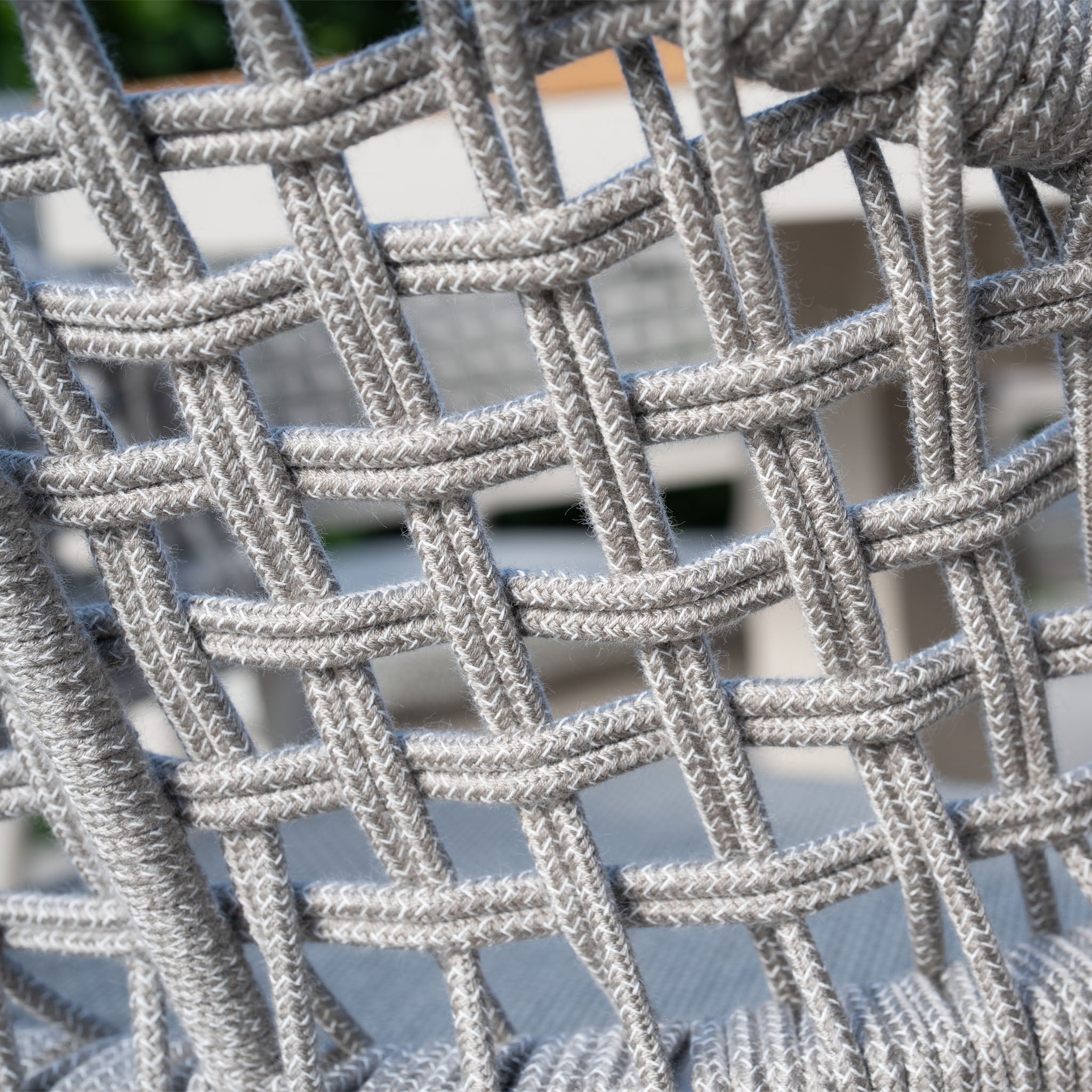 Close-up of a woven gray rope chair showcasing an intricate crisscross pattern, featured in the weatherproof aluminum Kalama 8 Seat Rectangular Dining Set with Teak Table in Latte, with a blurred background.