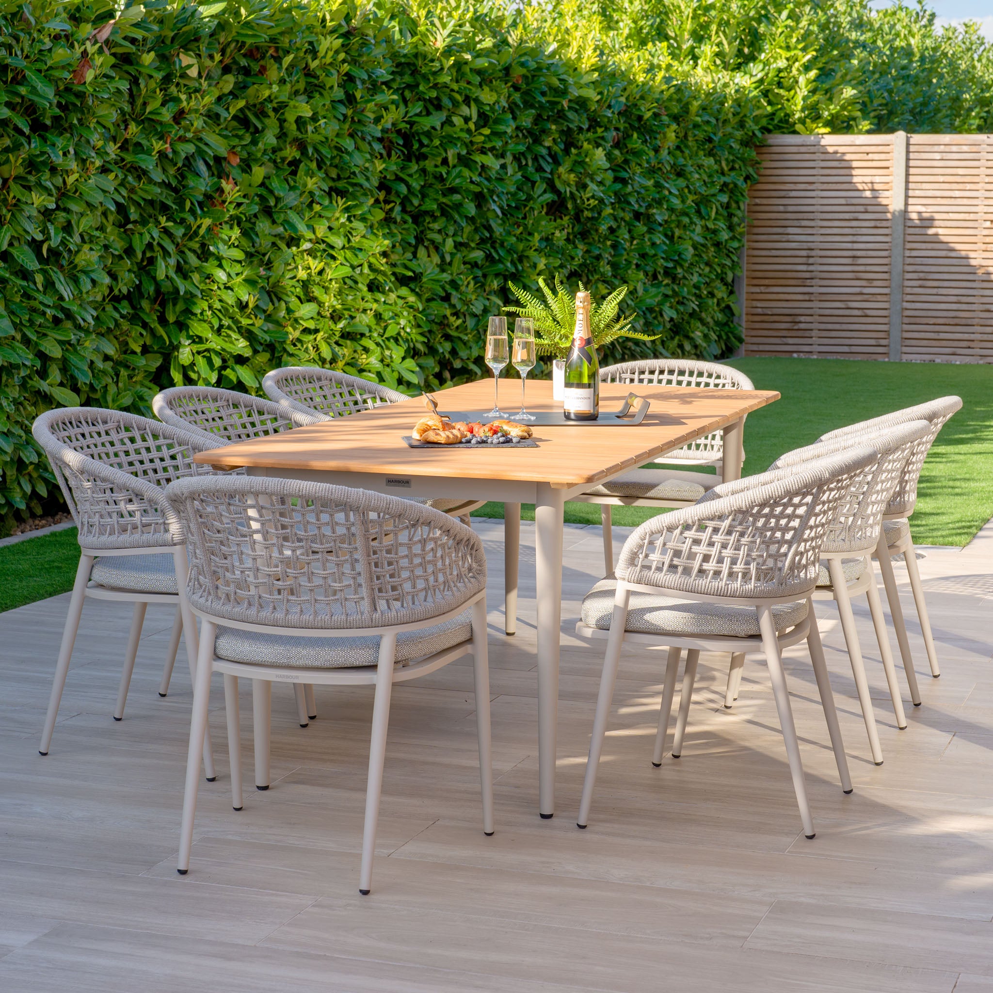 The Kalama 8 Seat Rectangular Dining Set with Teak Table in Latte features a chic teak table paired with eight woven chairs, making it perfect for hosting gatherings. Savor wine and snacks on the patio amidst greenery, as the weatherproof aluminum enhances durability.