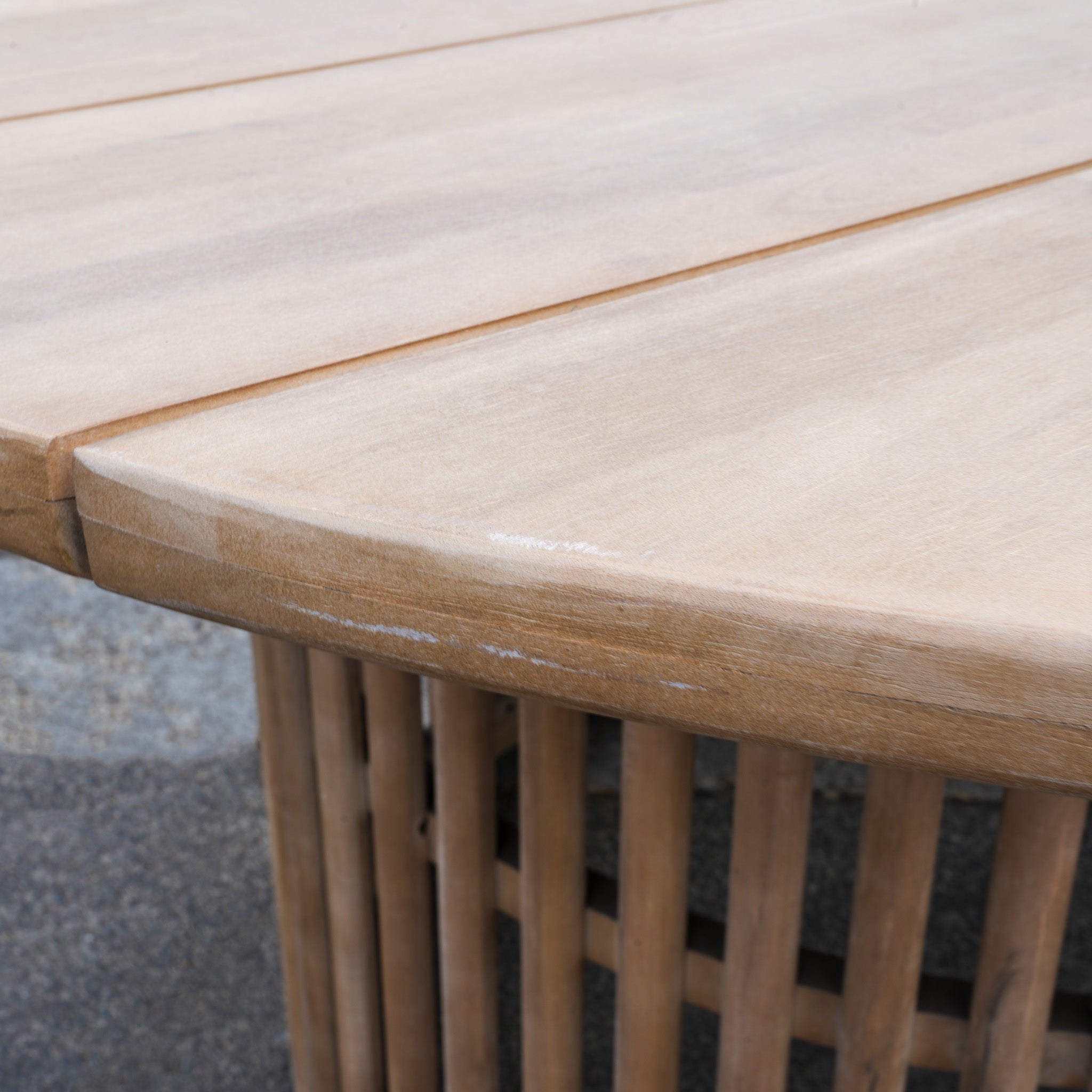 Close-up of a light Acacia wood table with rounded edge and vertical slats, from the Paia 8 Seat Round Dining Set (Ex Display), ideal for outdoor gatherings with water-resistant cushions.