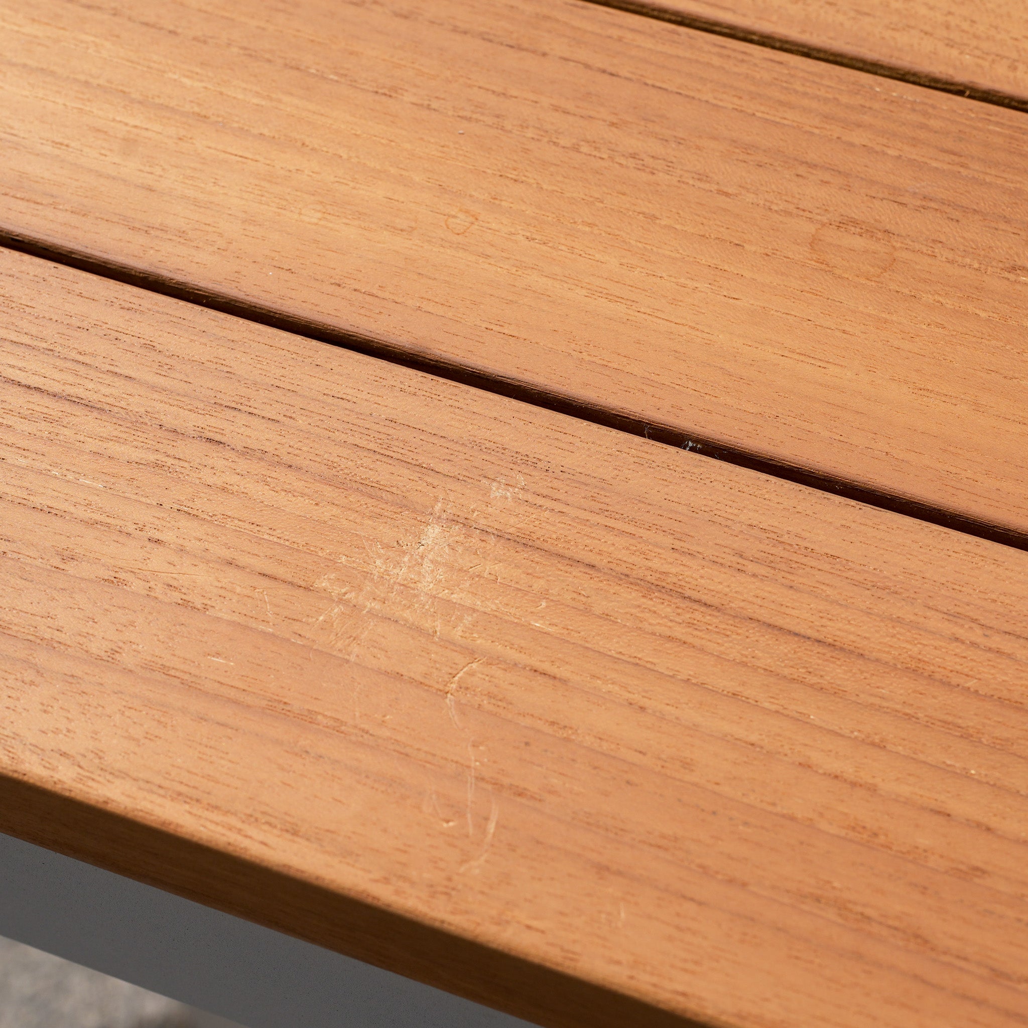 Close-up of the teak surface on the Cloverly 8 Seat Rectangular Teak Firepit Dining Set in Latte (Ex Display), showing visible wood grain and a light scratch mark, similar to finishes seen on premium firepit tables.