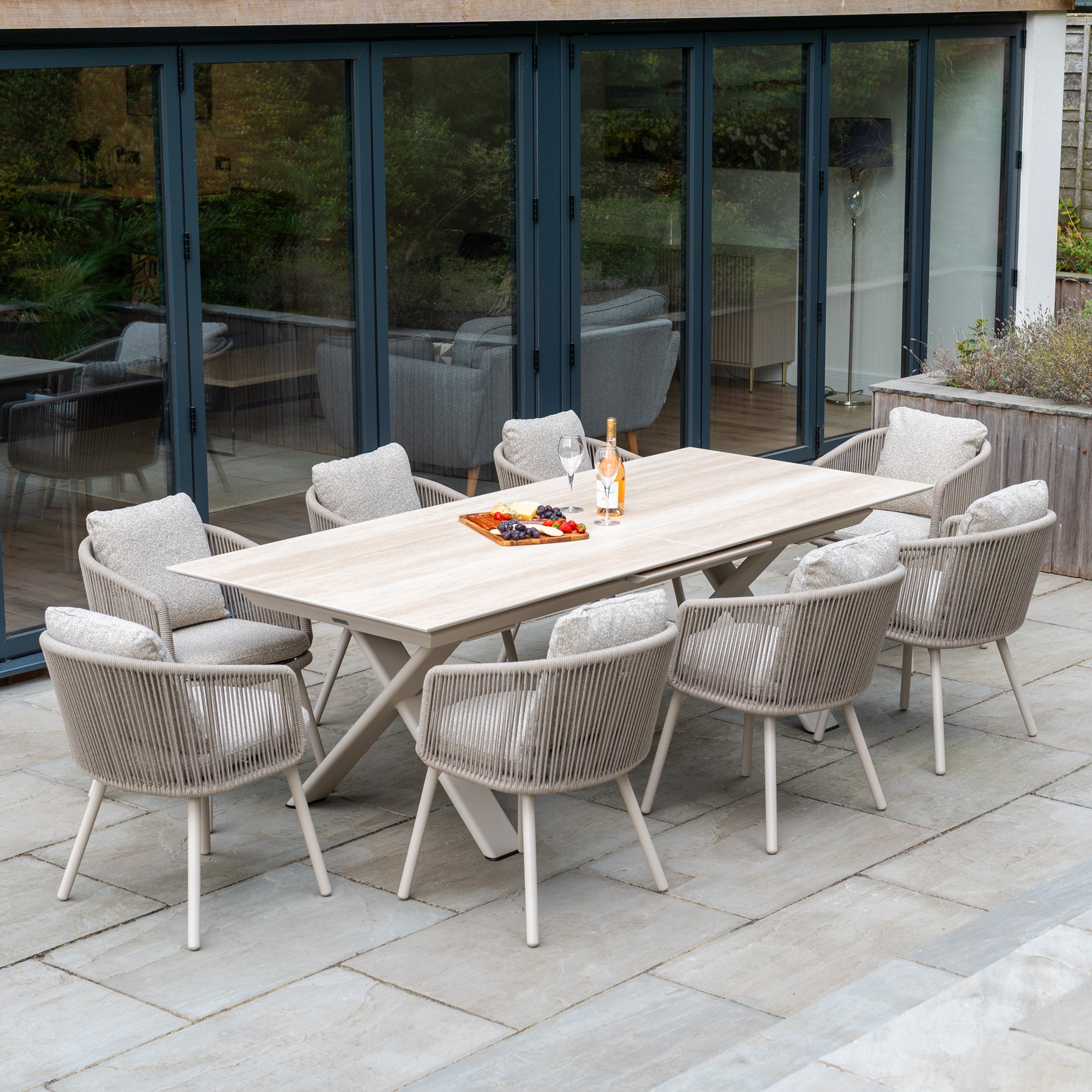 The Theia 8 Seat Rope Dining Set with Albatross Extending Table in Oatmeal includes eight cushioned chairs, perfect for enjoying wine and snacks on a stylish patio.
