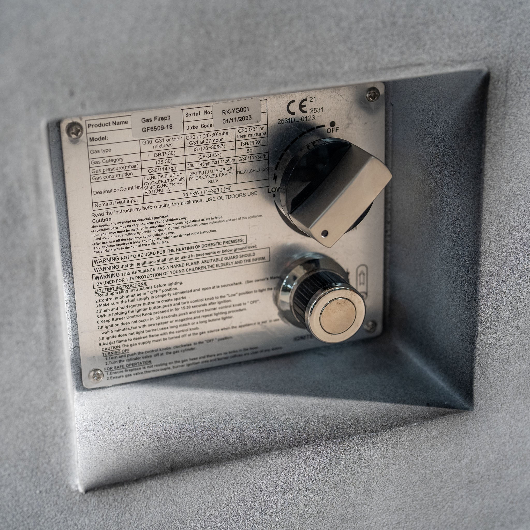 Close-up of the gas fireplace control panel on the Ember Rectangular Firepit Coffee Table in Stone Grey, featuring a silver knob, a black knob, and instructional text on a 304 stainless steel plate.