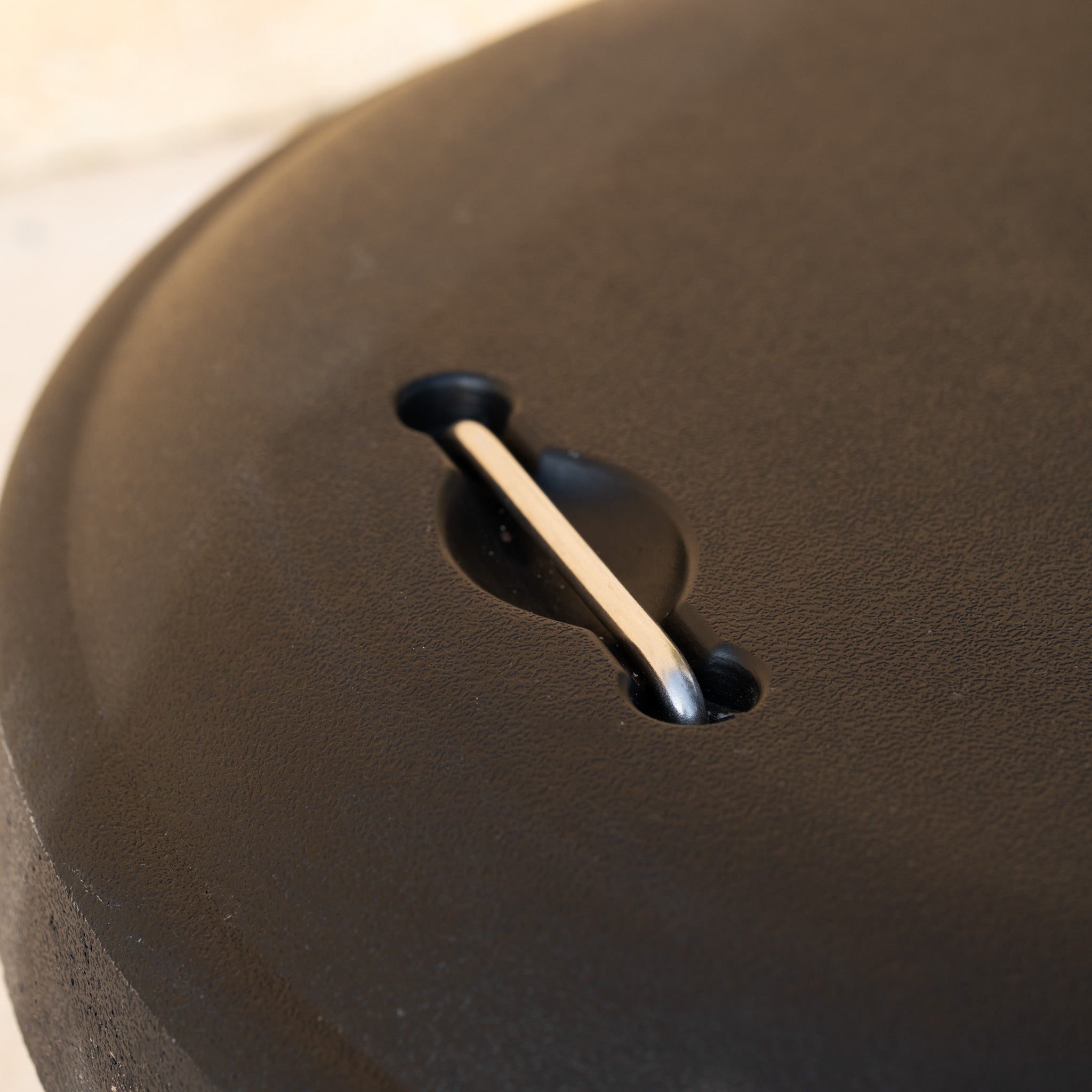 Close-up of a 50kg Concrete Parasol Base with Handles & Wheels, its sleek black surface showing a coin slot with a single coin halfway inserted.