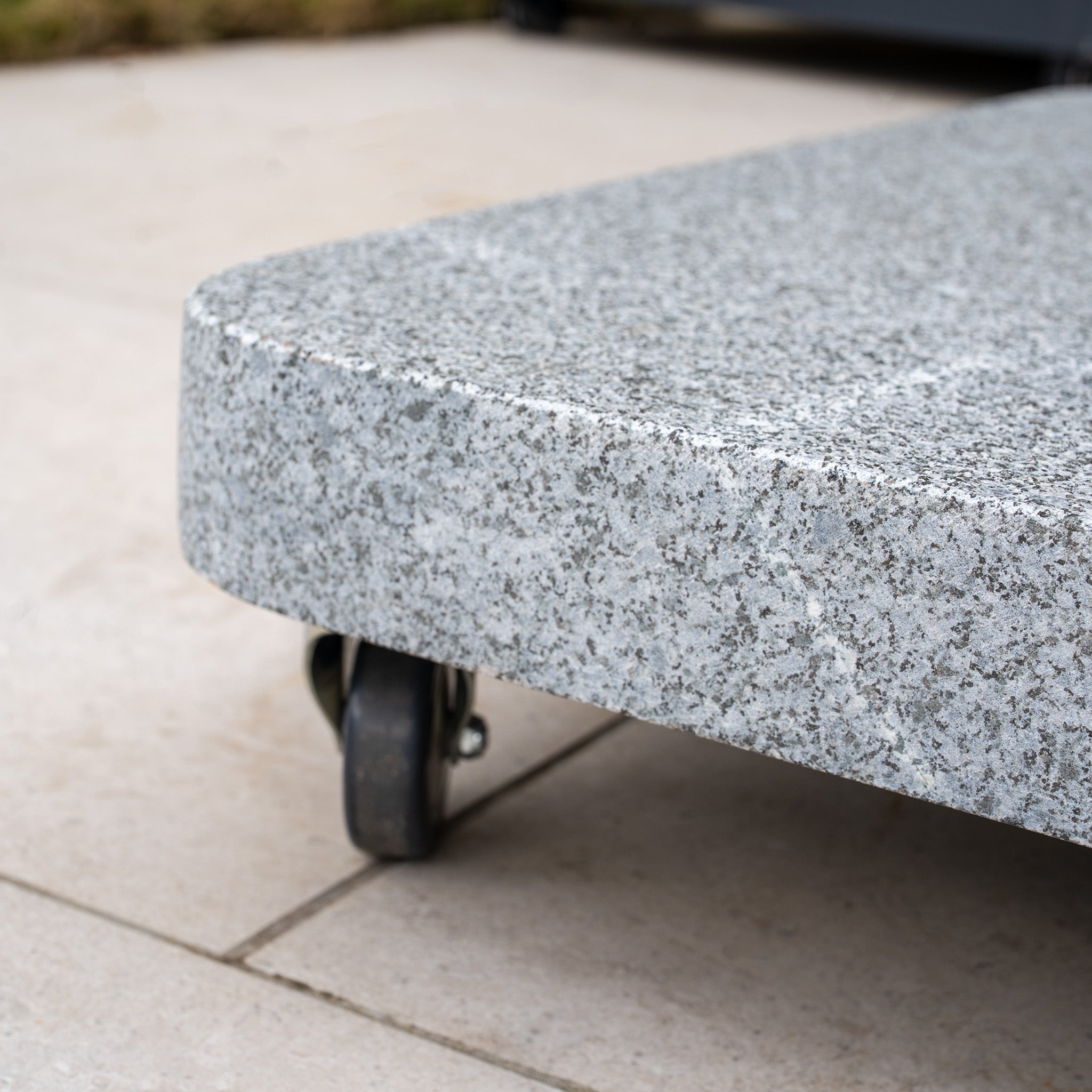 Close-up of the Siesta 125kg Granite Base in gray with small wheels on a tiled outdoor surface, ideal for supporting innovative cantilever designs or outdoor parasols.