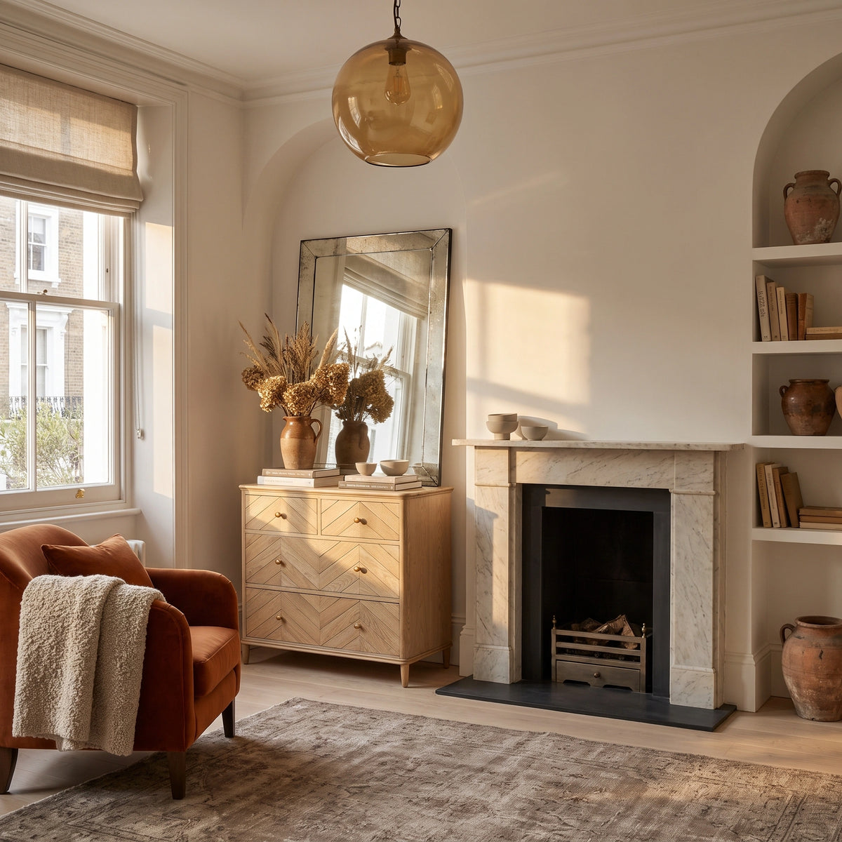 Cozy living room with a Hadley Herringbone 2 Over 2 Chest of Drawers in Natural, an armchair, mirror, fireplace, shelves, and dried flowers in neutral tones.