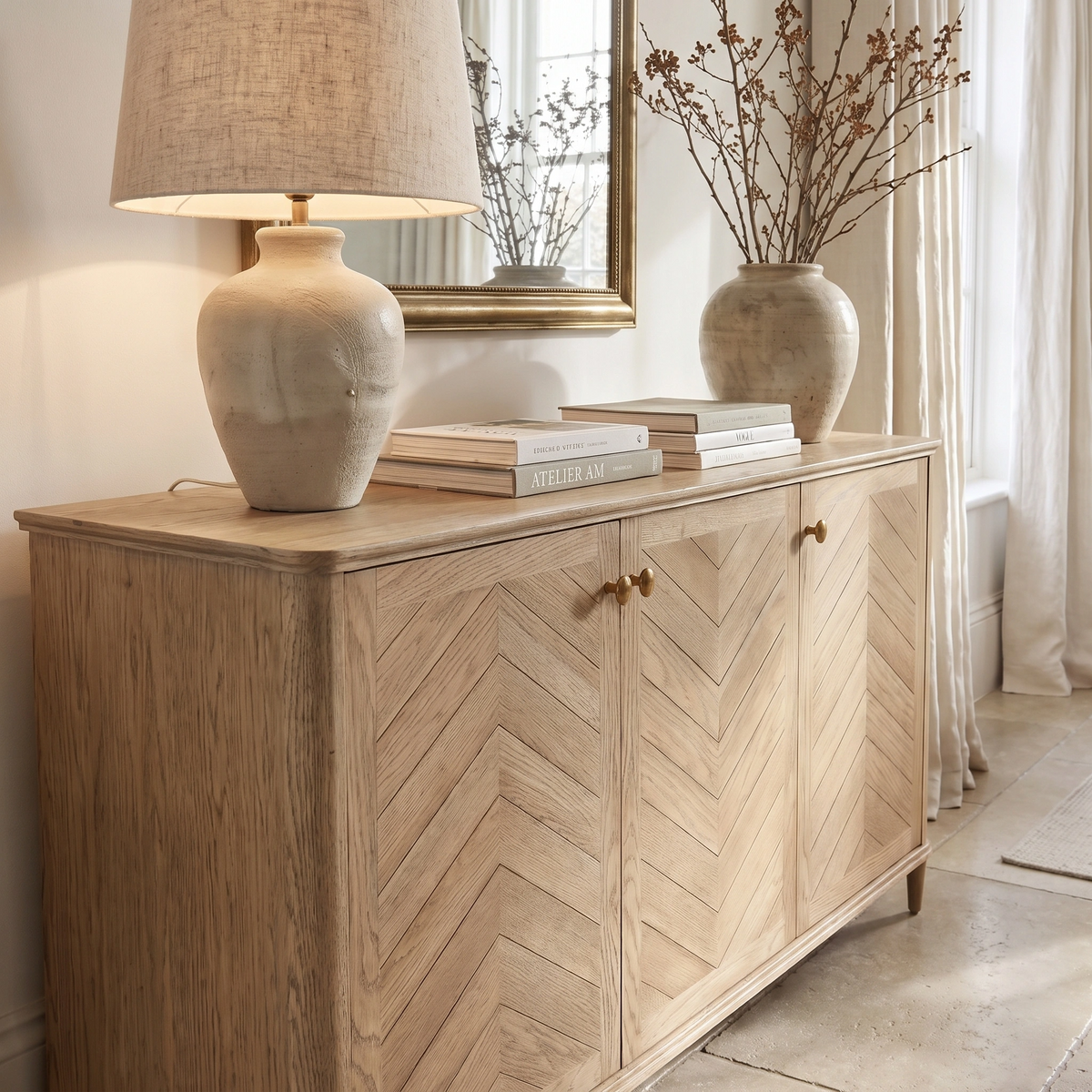 Hadley Herringbone 3 Door Sideboard in Natural with chevron pattern, styled with a lamp, vase of branches, books, and a mirror above.