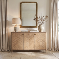 Hadley Herringbone 3 Door Sideboard in Natural styled with a lamp, vase filled with branches, books, and topped with a mirror in a bright room.