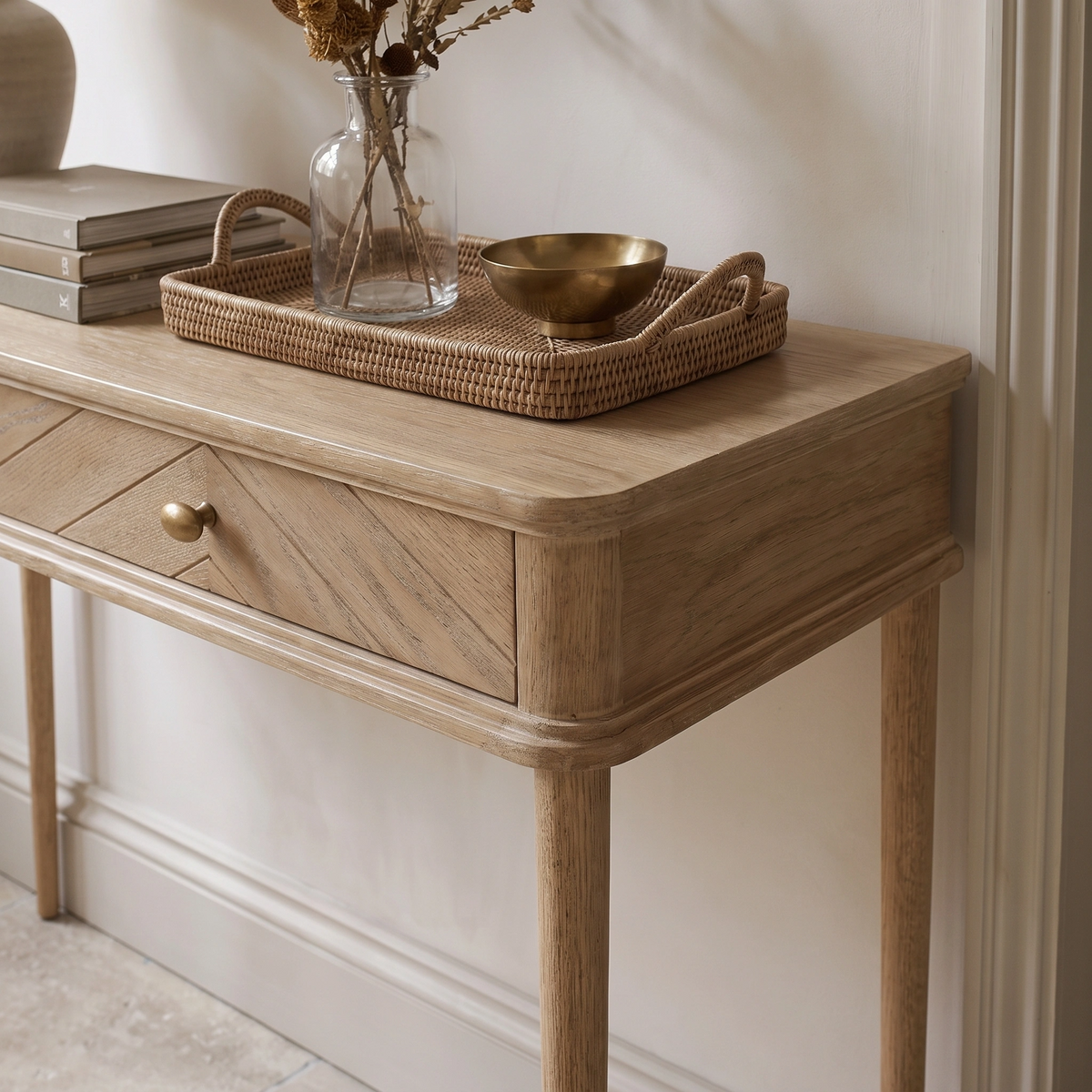 Hadley Herringbone Console Table in Natural styled with a drawer, tray, glass vase filled with dried flowers, and a brass bowl.