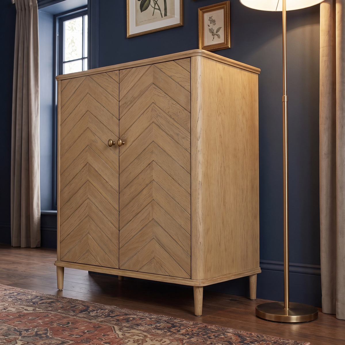 The Hadley Herringbone Drinks Cabinet in Natural with chevron-patterned doors stands beside a tall floor lamp in a cozy, blue-walled room.