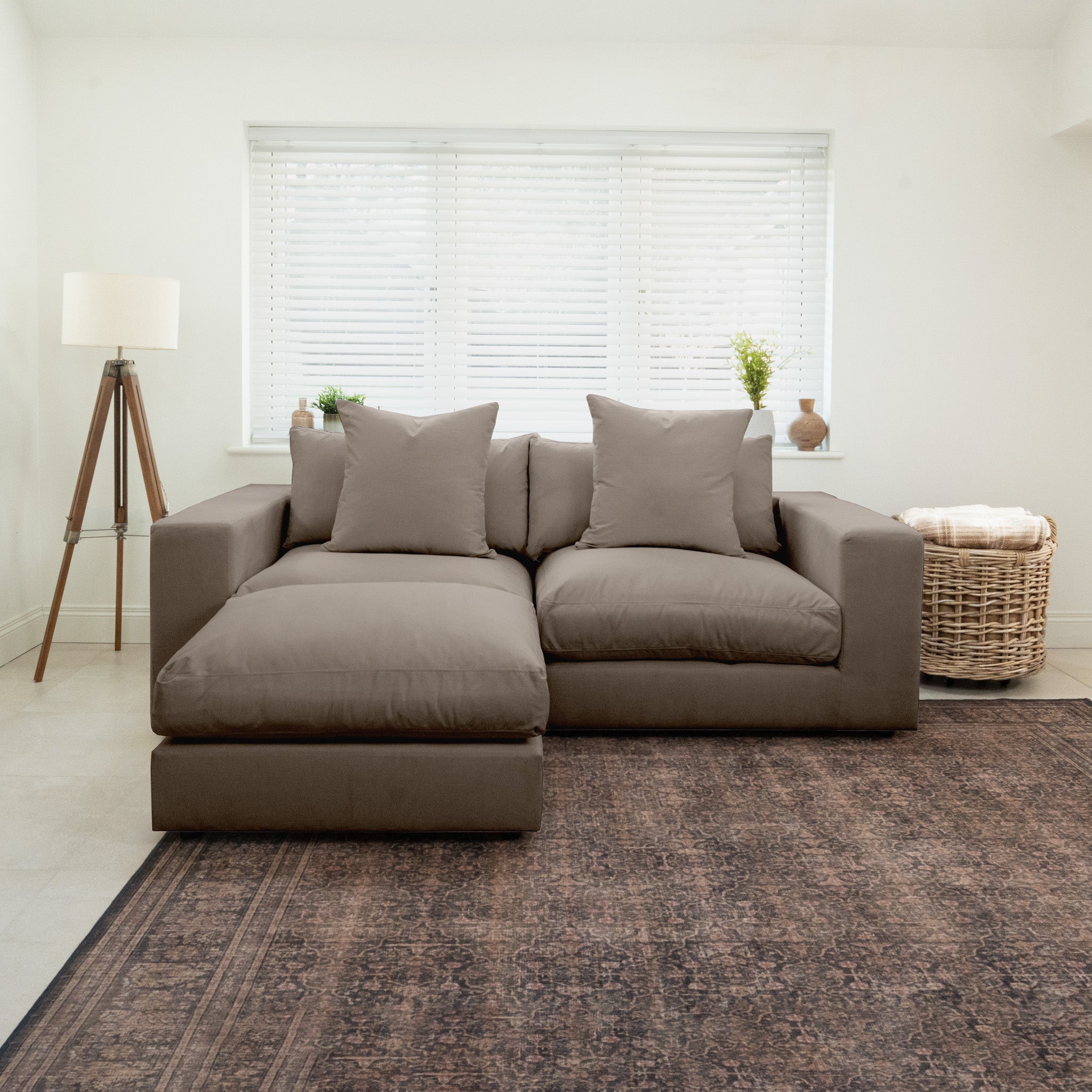 The Hampshire Modular 2 Seat Sofa in Cocoa with duck feather cushions is placed in a bright, minimalist living room with a rug and large window blinds.