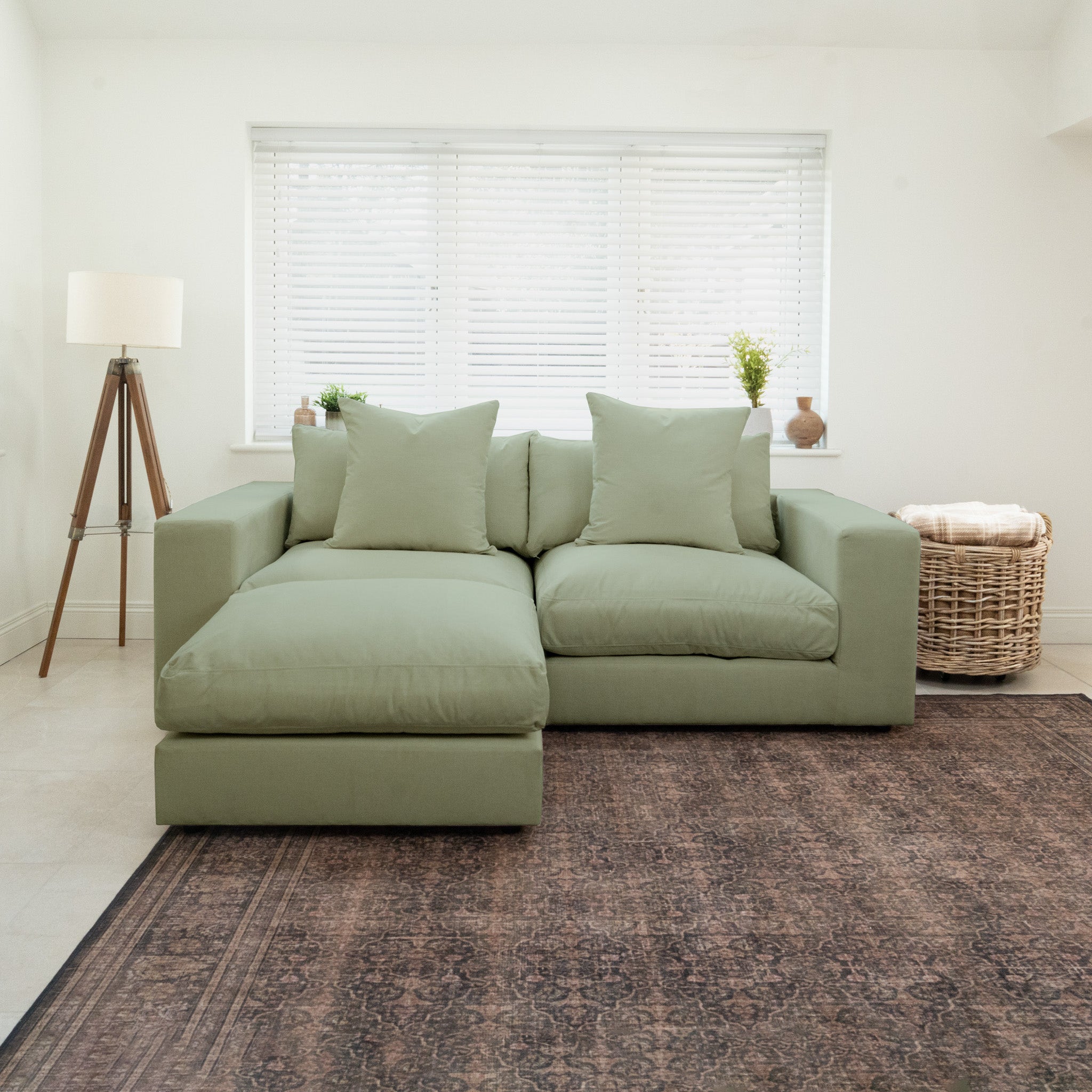 Hampshire Modular 2 Seat Sofa in Moss Green with duck feather and down cushions, placed in a bright room by a window, rug, lamp, and wicker basket.