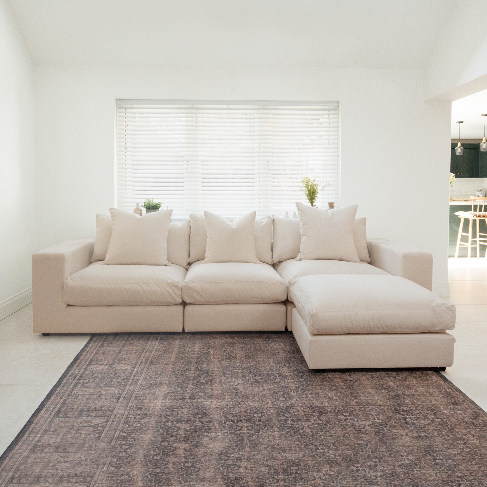The Hampshire Modular 3 Seat Sofa in Beige features luxurious duck feather cushions and is crafted from sustainably sourced hardwood for lasting style and comfort. Shown on a patterned rug with white blinds in the background.