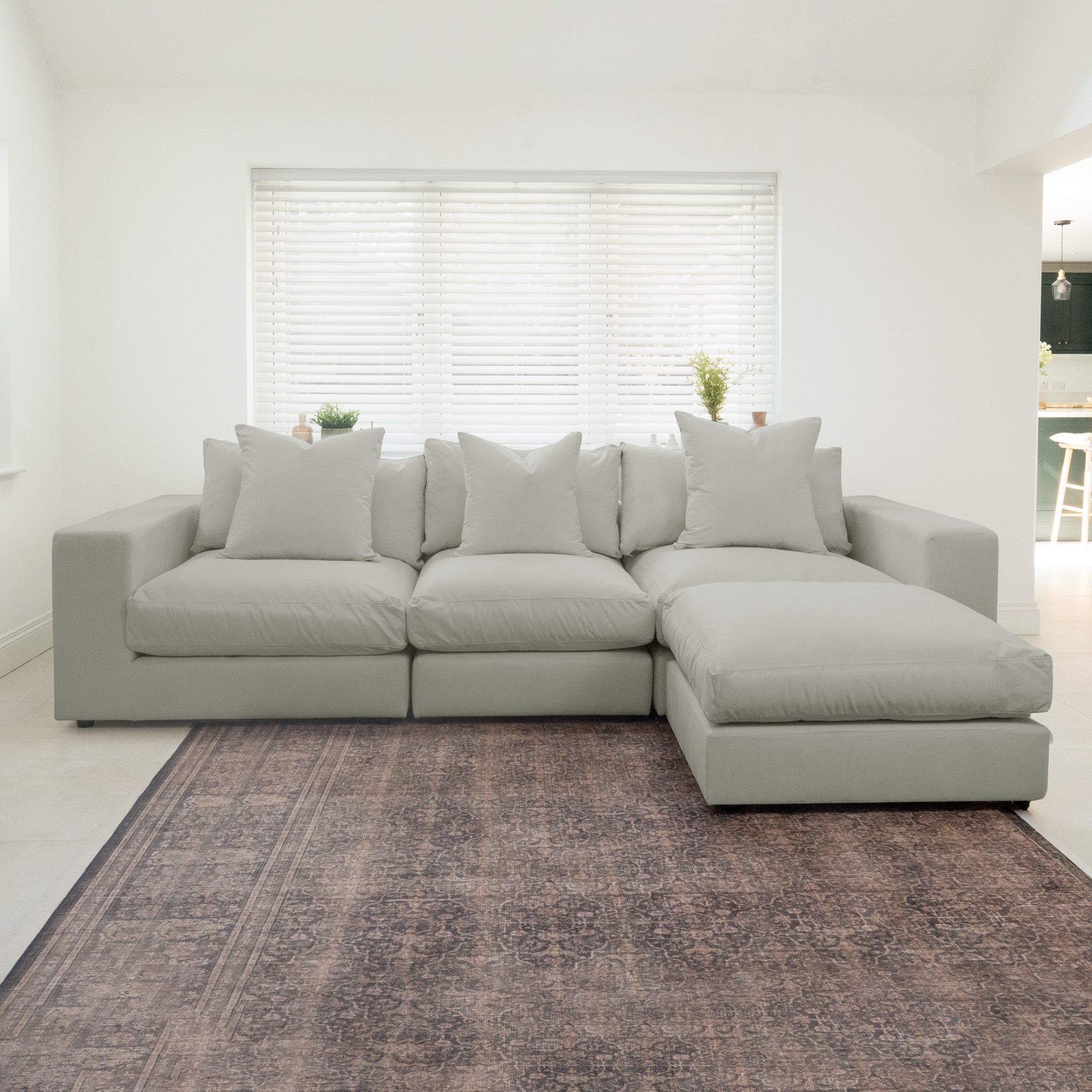 The Hampshire Modular 3 Seat Sofa in Classic Grey, featuring plush duck feather cushions and crafted from sustainably sourced hardwood, sits on a large patterned rug in a bright room with white blinds.