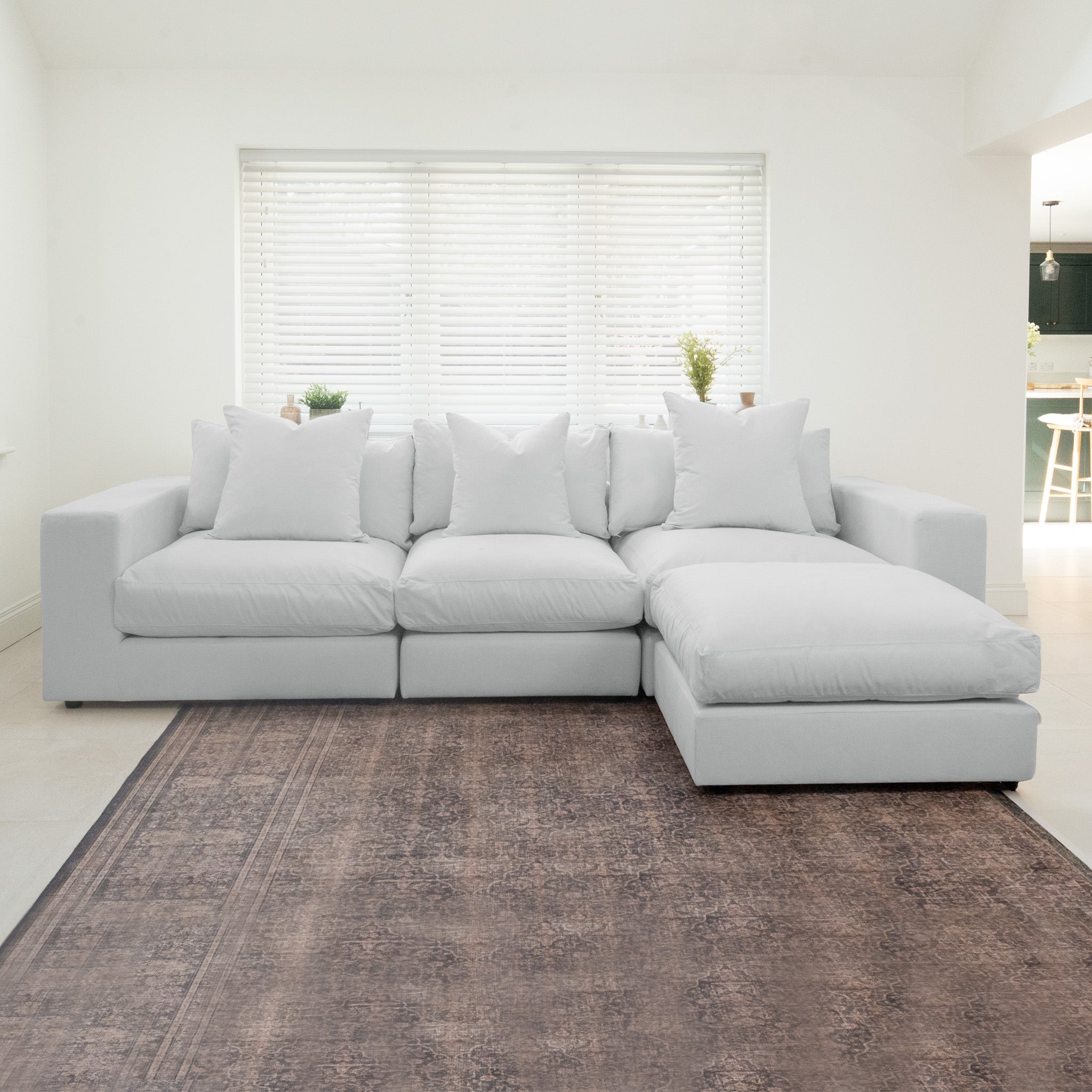 The Hampshire Modular 3 Seat Sofa in Dove Grey with duck feather cushions sits on a dark rug in a bright room with large windows and white blinds.