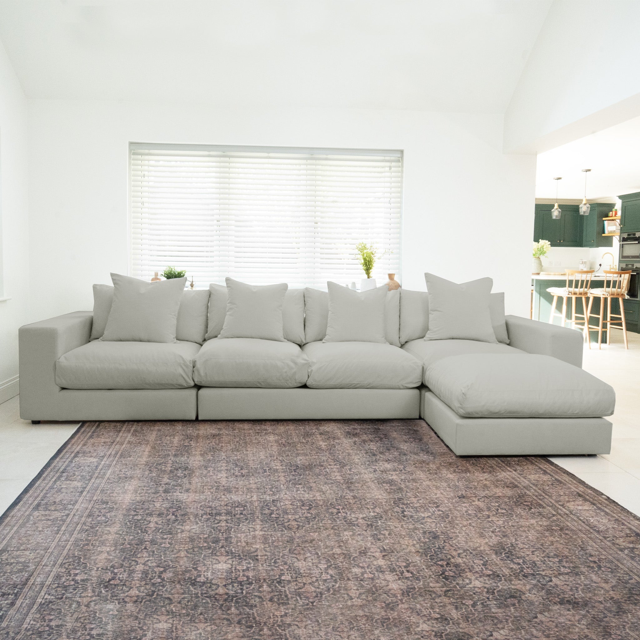 The Hampshire Modular 4 Seat Sofa in Classic Grey with plush duck feather cushions sits atop a patterned rug in a bright, modern living room.