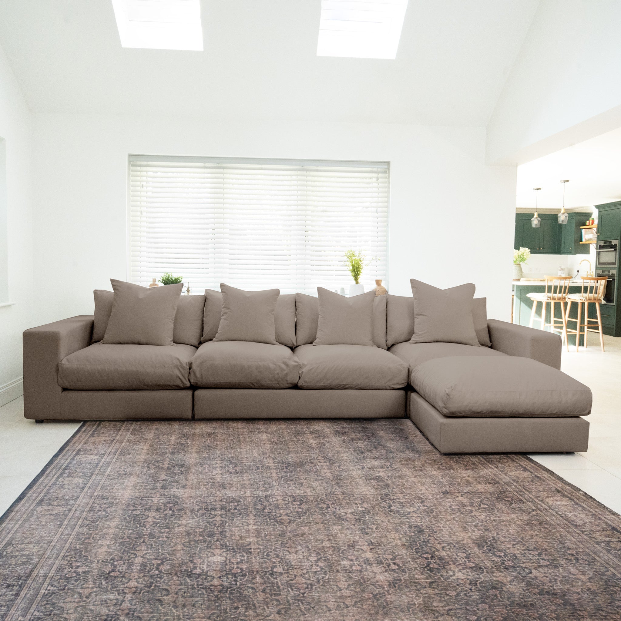 The Hampshire Modular 4 Seat Sofa in Cocoa, made from sustainable hardwood with six cushions, sits on a patterned rug in a bright, modern living room.