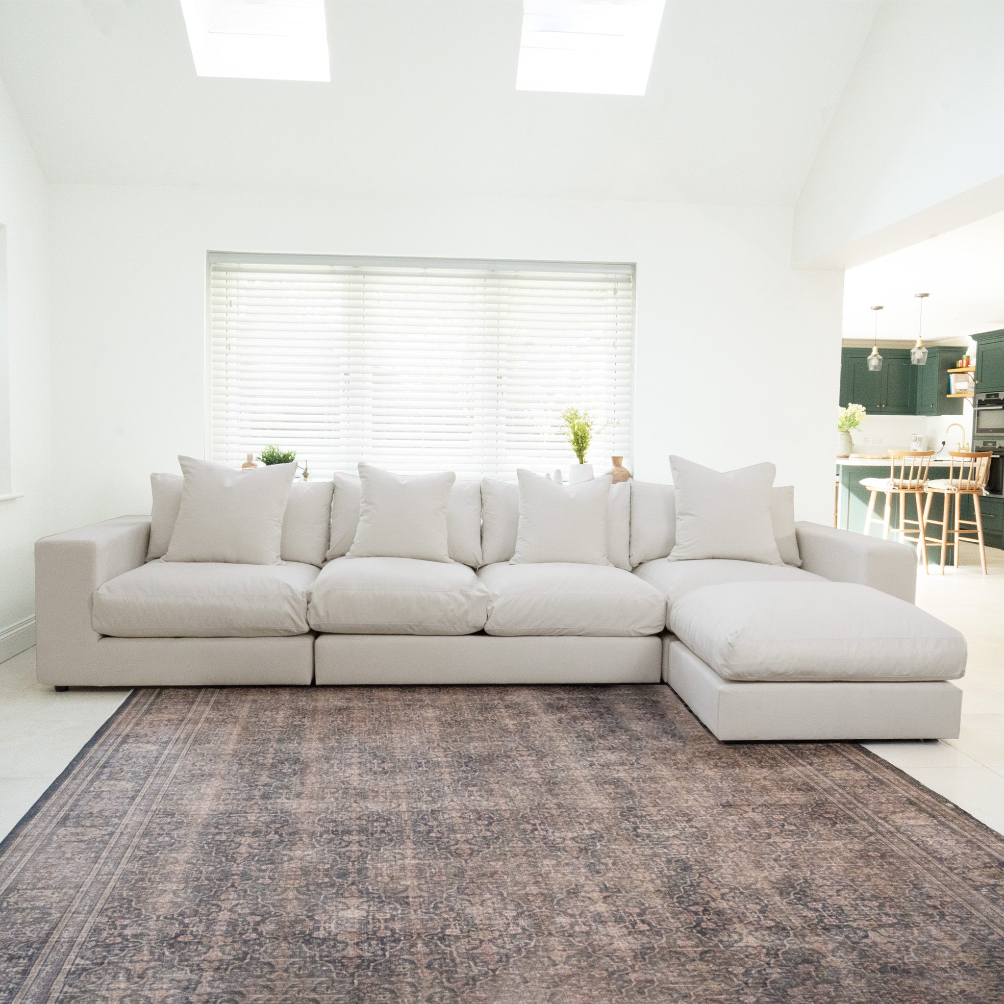 The Hampshire Modular 4 Seat Sofa in Warm Grey with plush cushions is placed on a patterned rug in a bright, modern living room.