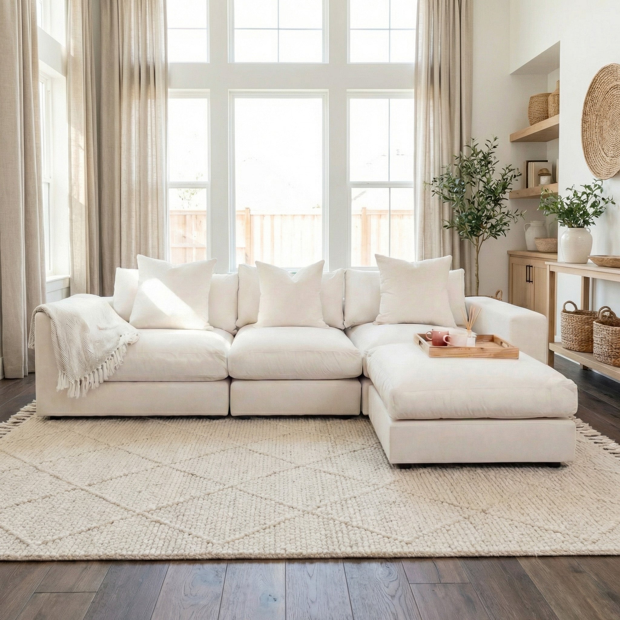 Bright living room with the Hampshire Modular 3 Seat Sofa in Ivory featuring duck feather cushions, a throw blanket, tray, large windows, and neutral decor.
