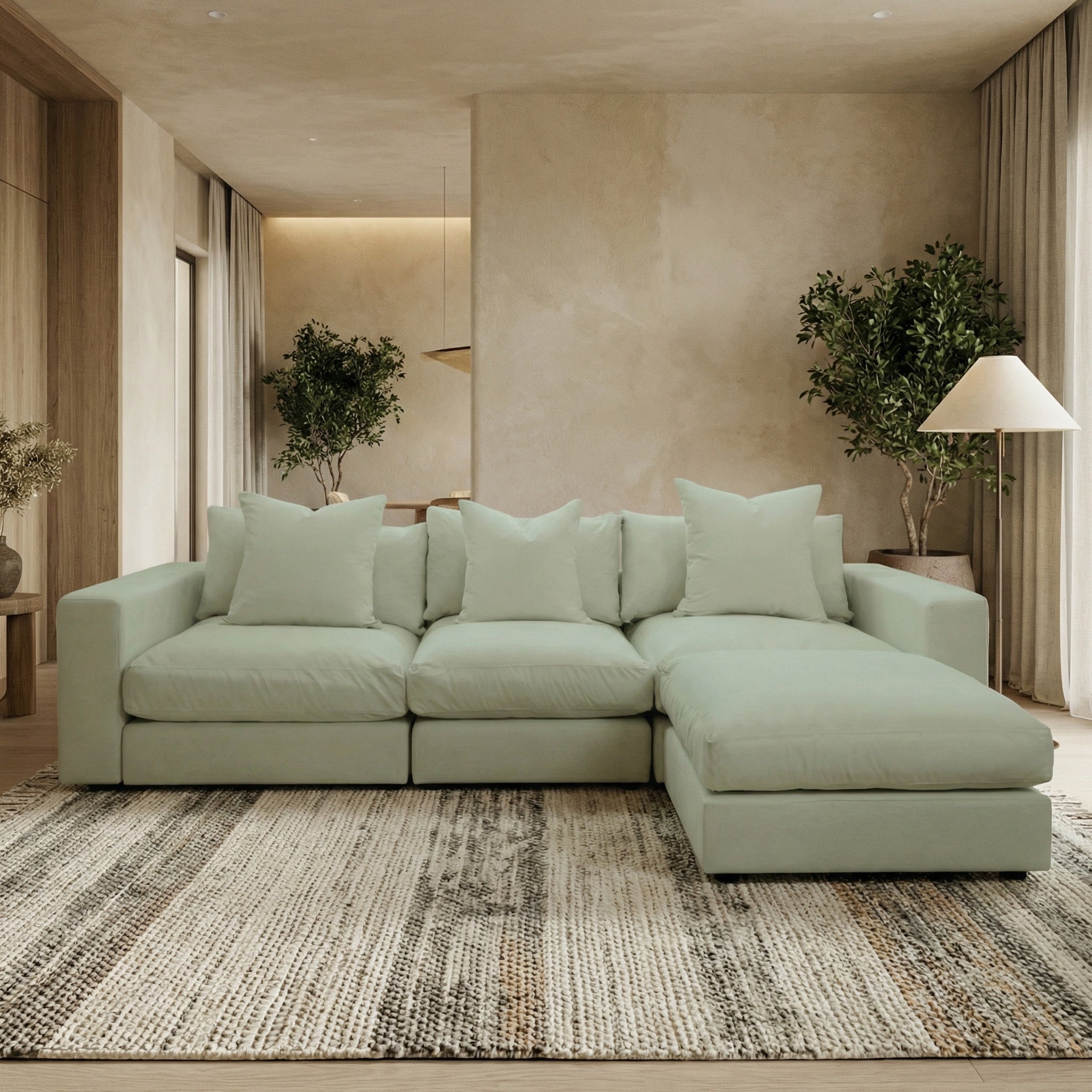 The Hampshire Modular 3 Seat Sofa in Moss Green, handmade in England with duck feather cushions, sits on a patterned rug in a modern living room featuring plants and neutral walls.