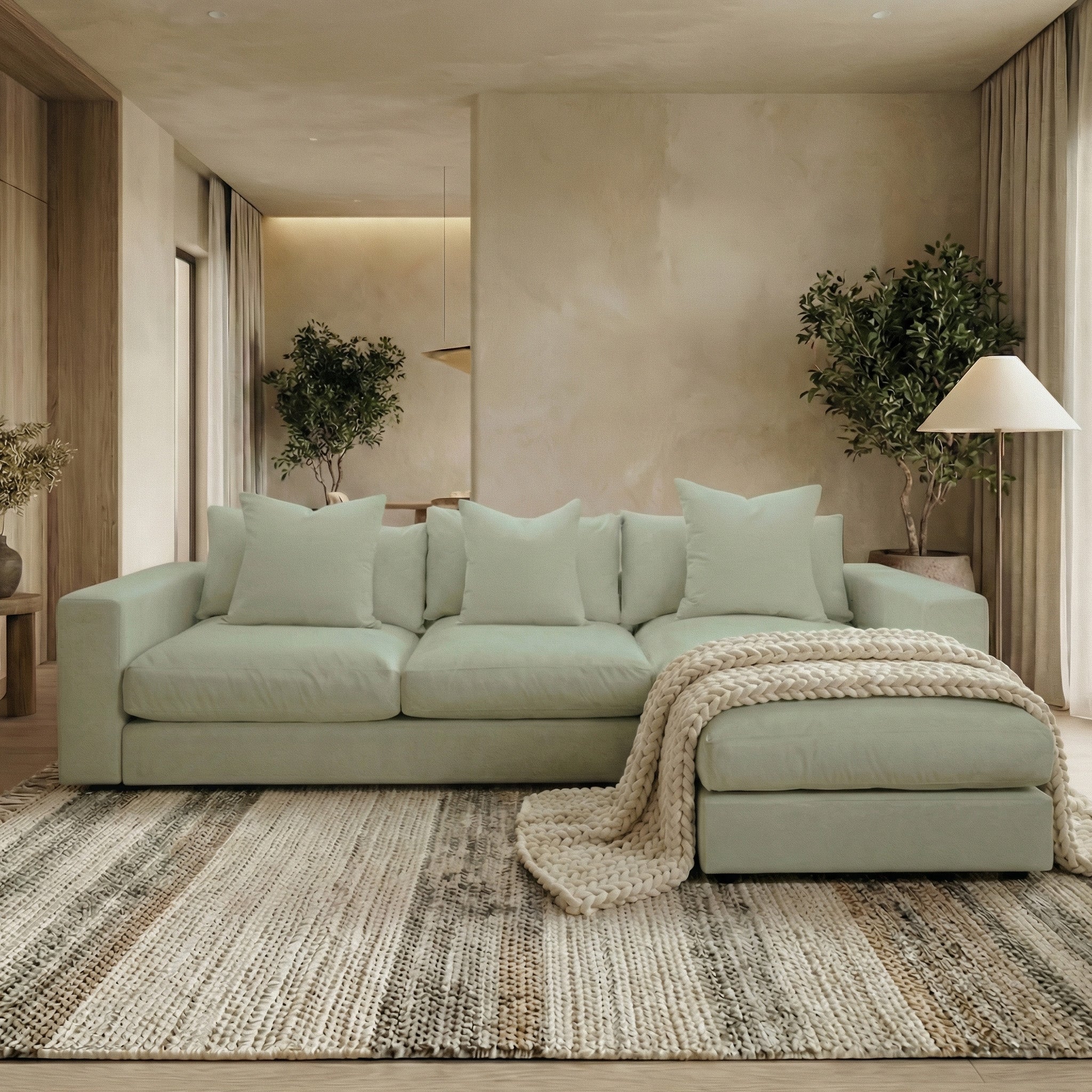 A modern living room with the Hampshire Modular 3 Seat Sofa in Moss Green featuring duck feather cushions, a throw blanket, potted plants, and a neutral rug.
