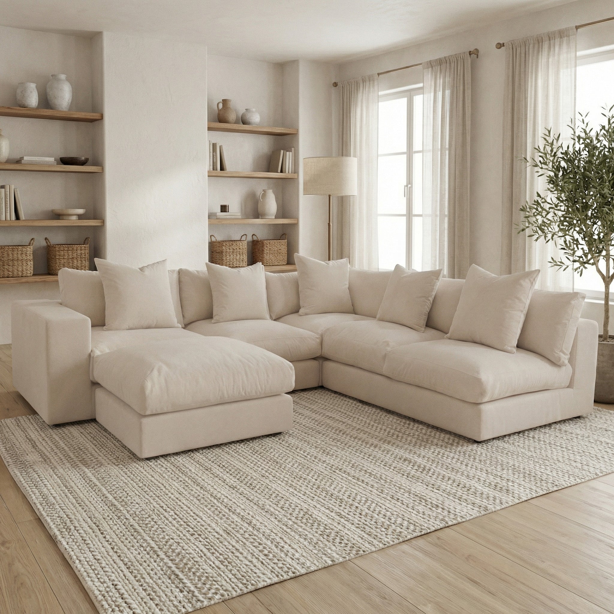The Hampshire Modular Corner Sofa in Beige sits on a textured rug in a bright, modern living room with shelves and large windows.