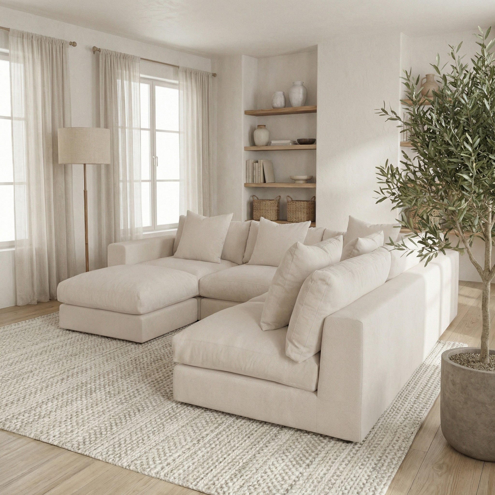 The Hampshire Modular Corner Sofa in Beige is featured in a bright living room with large windows, a floor lamp, shelves, and a potted plant.