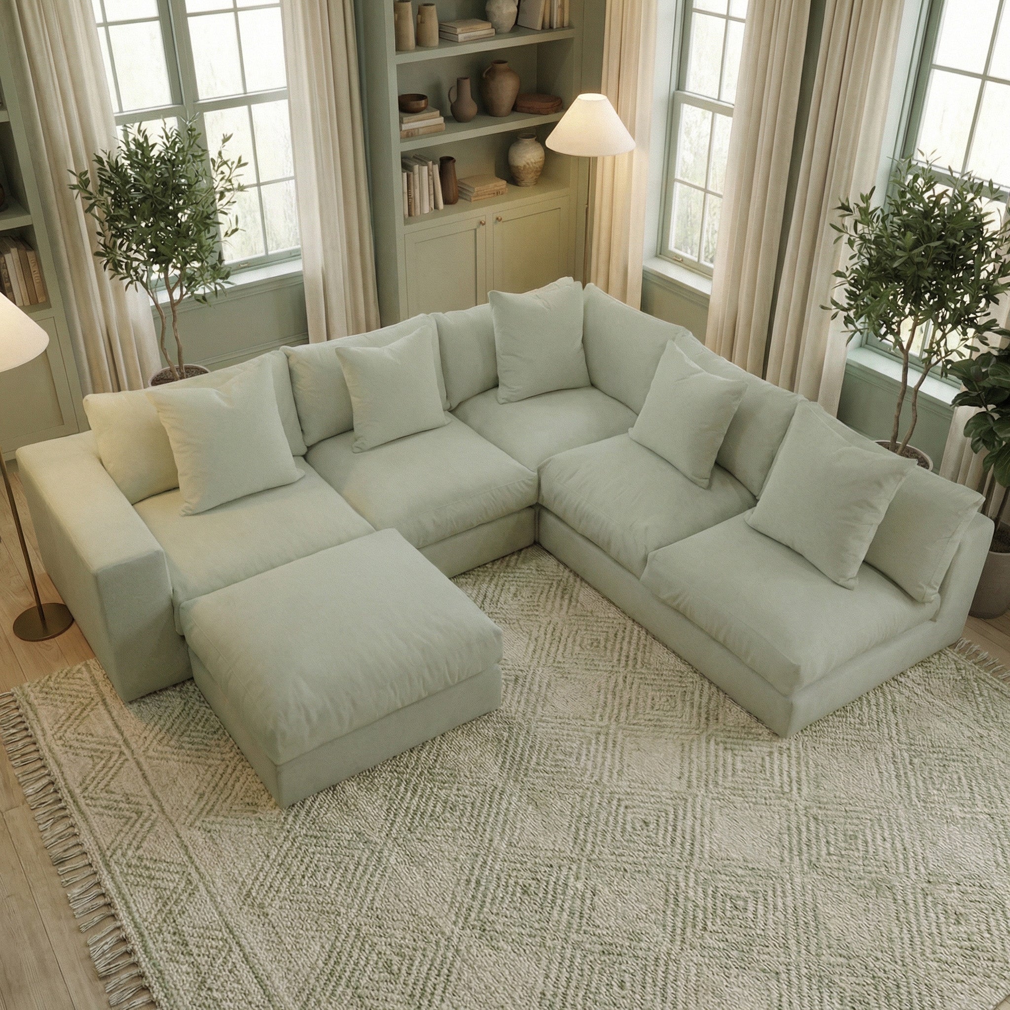 The Hampshire Modular Corner Sofa in Moss Green with a matching ottoman rests on a patterned rug in a cozy, sunlit living room, bringing handmade English comfort and charm to the space.