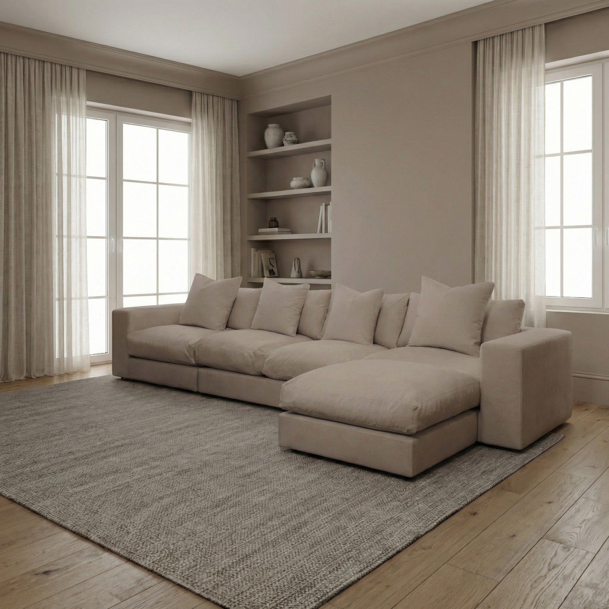 Modern living room with a Hampshire Modular 4 Seat Sofa in Cocoa featuring plush duck feather cushions, a gray rug, wood floor, shelves, and large curtained windows.