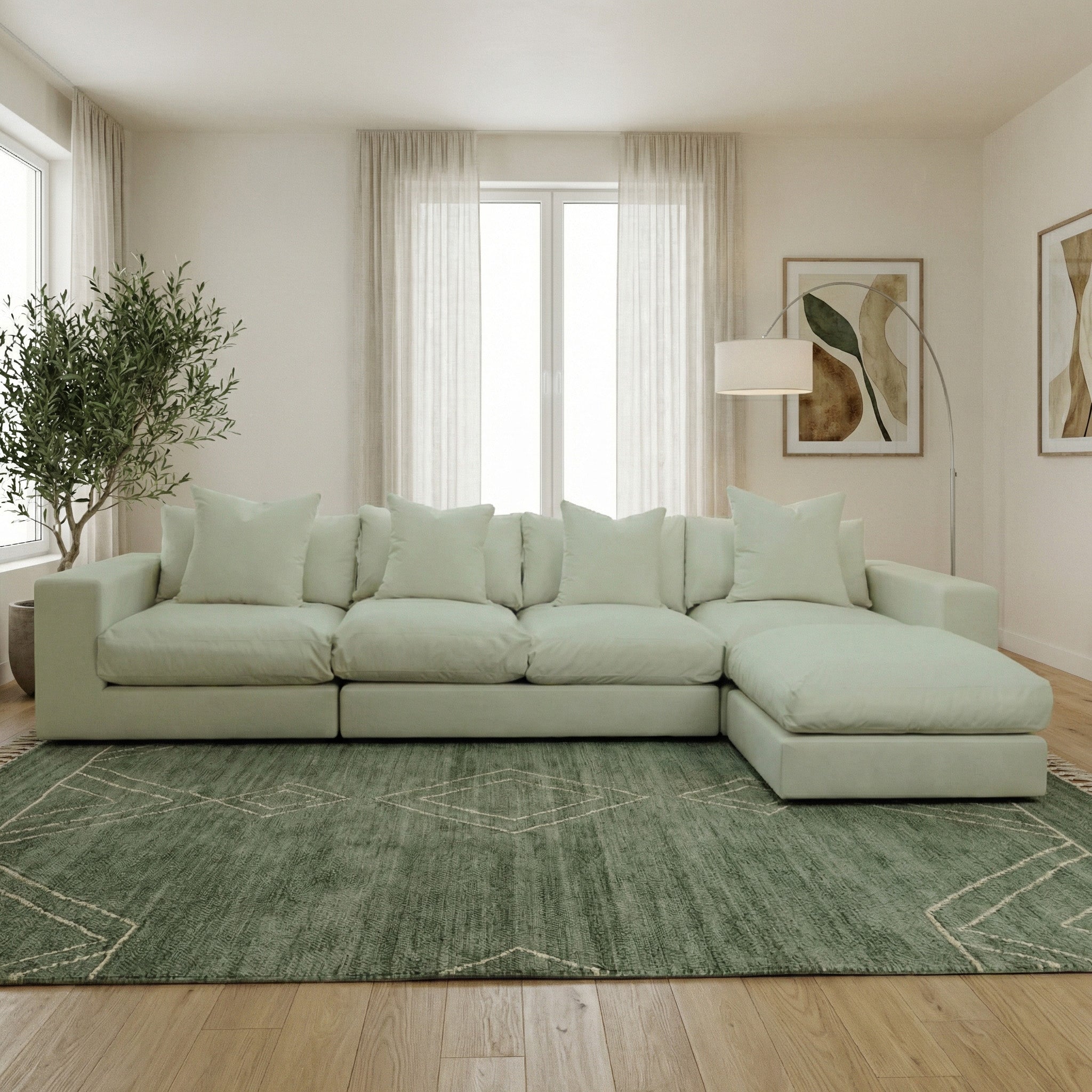 The Hampshire Modular 4 Seat Sofa in Moss Green, featuring duck feather cushions and pillows, sits on a green rug in a bright living room with art and sheer curtains.