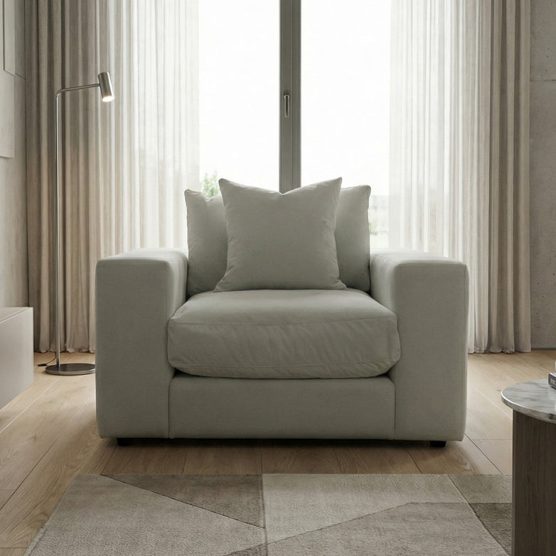 A Hampshire Modular Armchair in Classic Grey with feather and down cushions sits by a window with sheer curtains in a modern room.