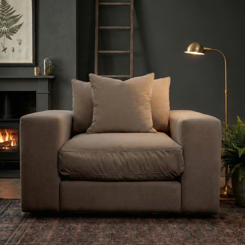 A Hampshire Modular Armchair in Cocoa with plush duck feather cushions sits by a fireplace in a modern living room with dark walls and stylish decor.