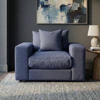 A Hampshire Modular Armchair in Midnight Blue with two duck feather and down cushions sits on a rug in front of a dark wall and an abstract painting.