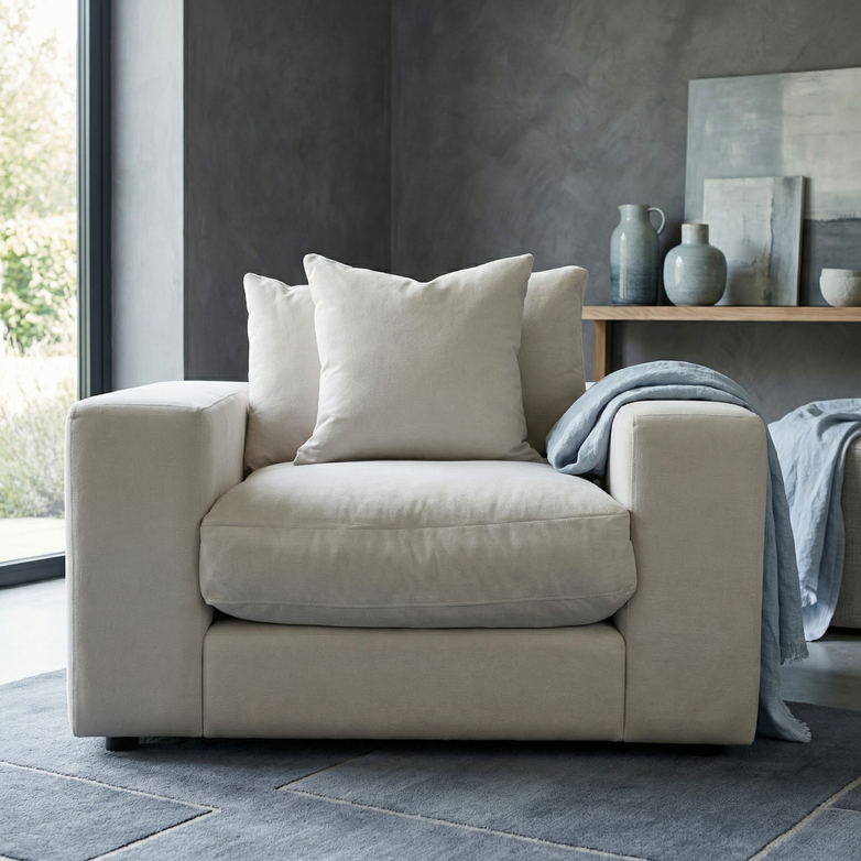 The Hampshire Modular Armchair in Warm Grey with duck feather cushions, two pillows, and a blue throw sits in a modern living room featuring ceramic vases on a console table.