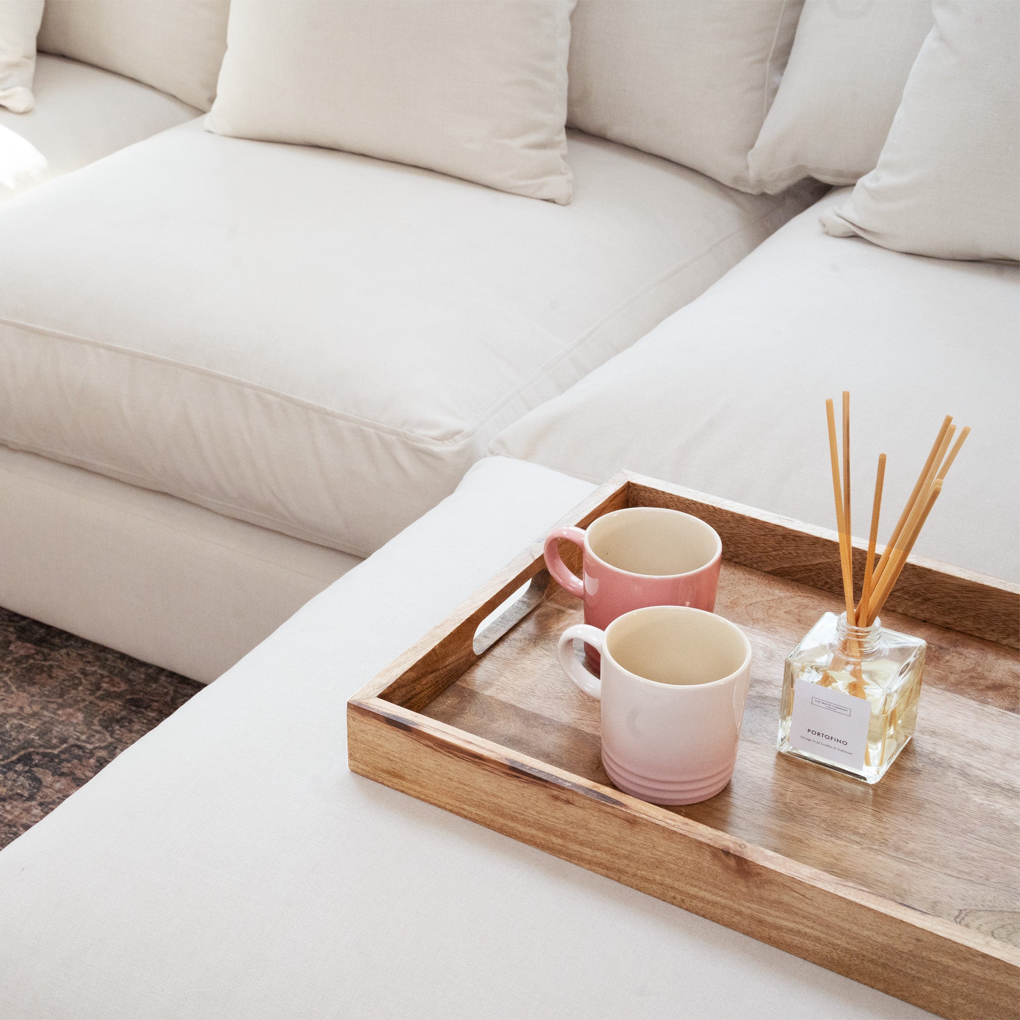 Wooden tray with two mugs and a reed diffuser on an ivory Hampshire Modular Corner Sofa, crafted from sustainably sourced hardwood.