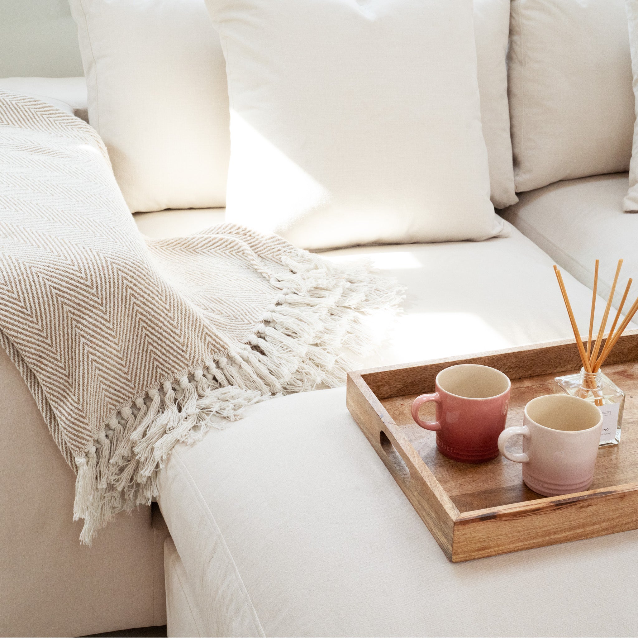 Ivory Hampshire Modular Corner Sofa styled with a fringed throw blanket, plush duck feather and down cushions, plus a wooden tray featuring two mugs and a reed diffuser.