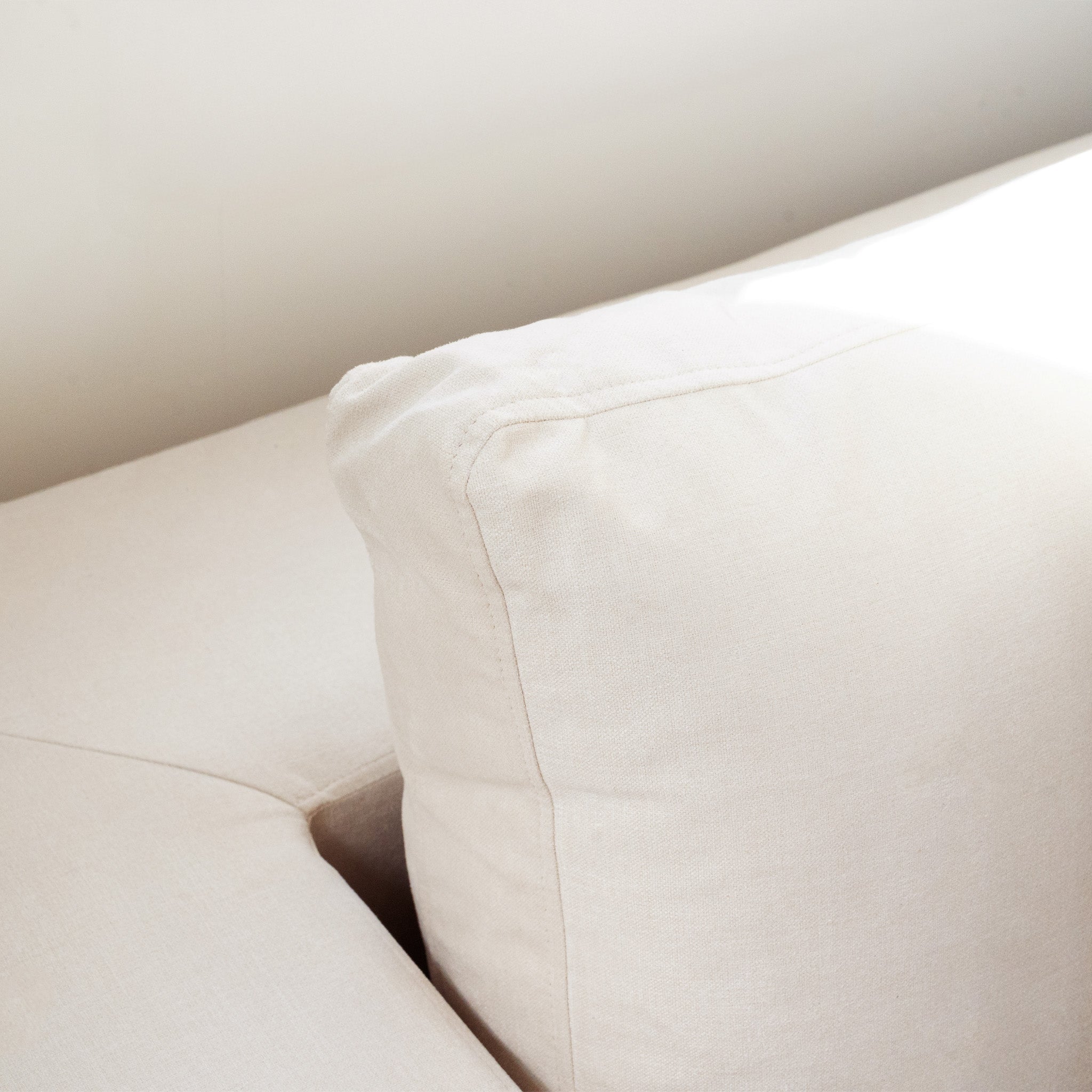Close-up of the Hampshire Modular Corner Sofa in Ivory, featuring a cushion filled with luxurious duck feather and down, set against a plain, light-colored wall.