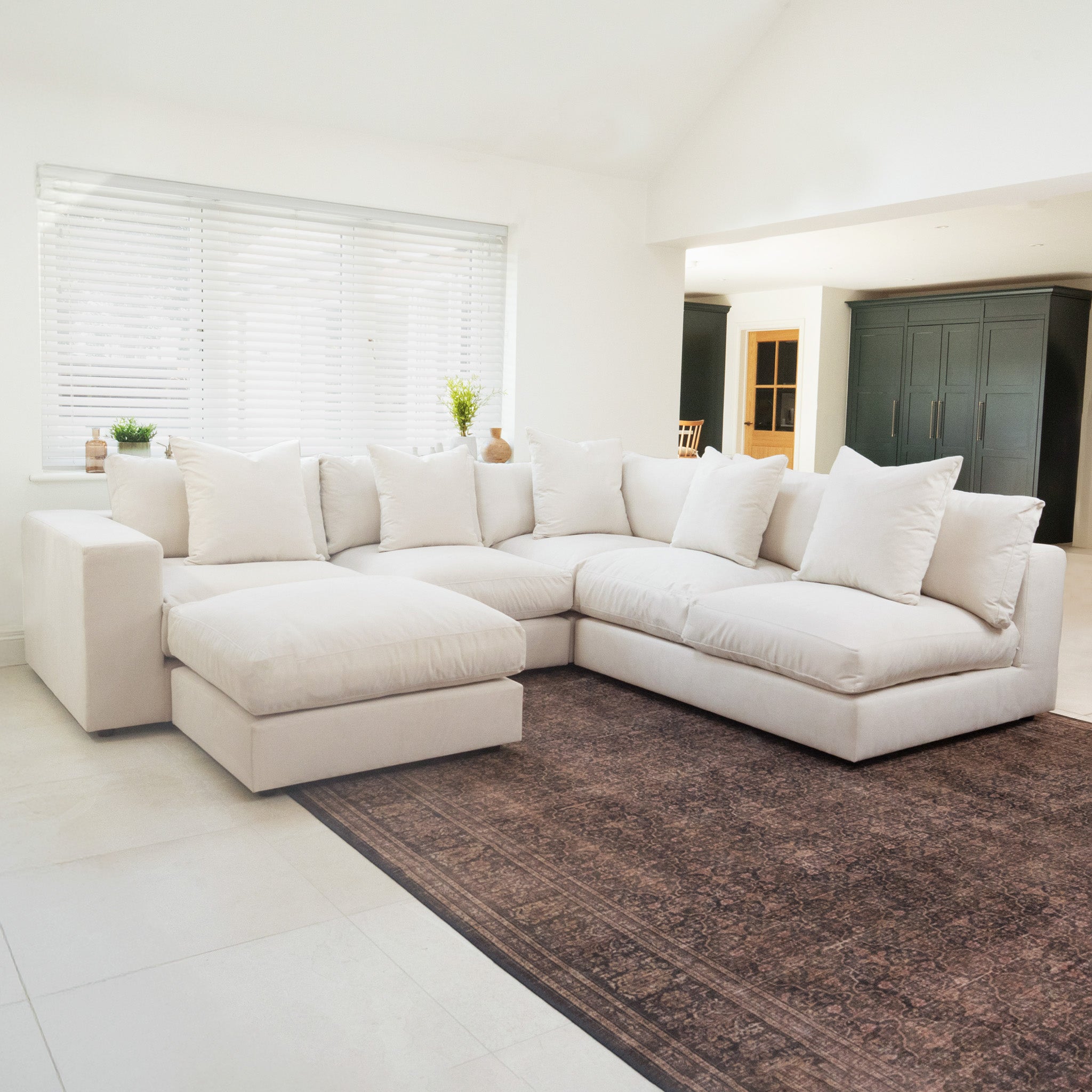 The Hampshire Modular Corner Sofa in Ivory features luxurious duck feather and down cushions, set on a brown rug in a bright, modern living room. Crafted from sustainably sourced hardwood for lasting elegance and comfort.