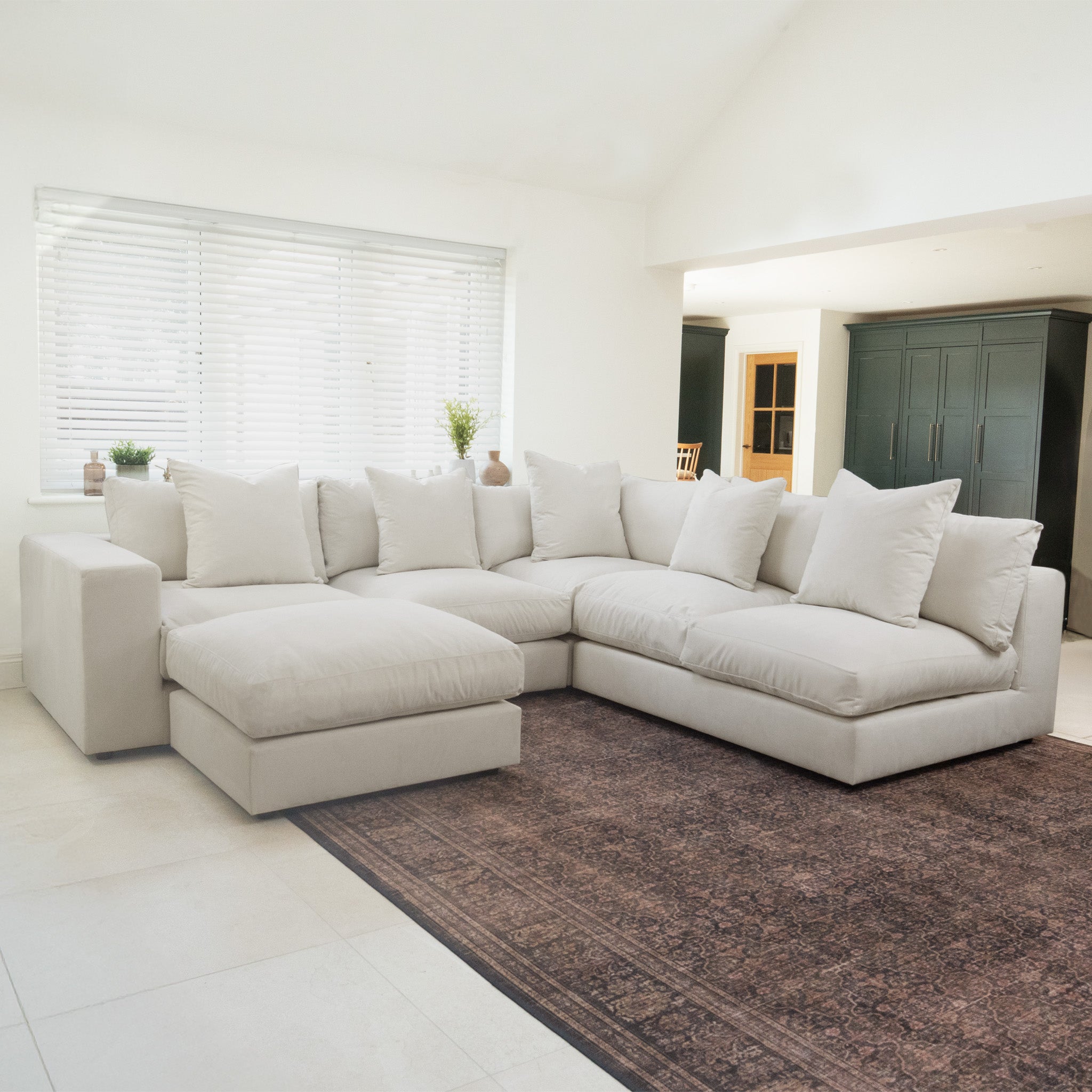 The warm grey Hampshire Modular Corner Sofa with luxurious duck feather cushions sits on a brown rug in a bright, modern living room.