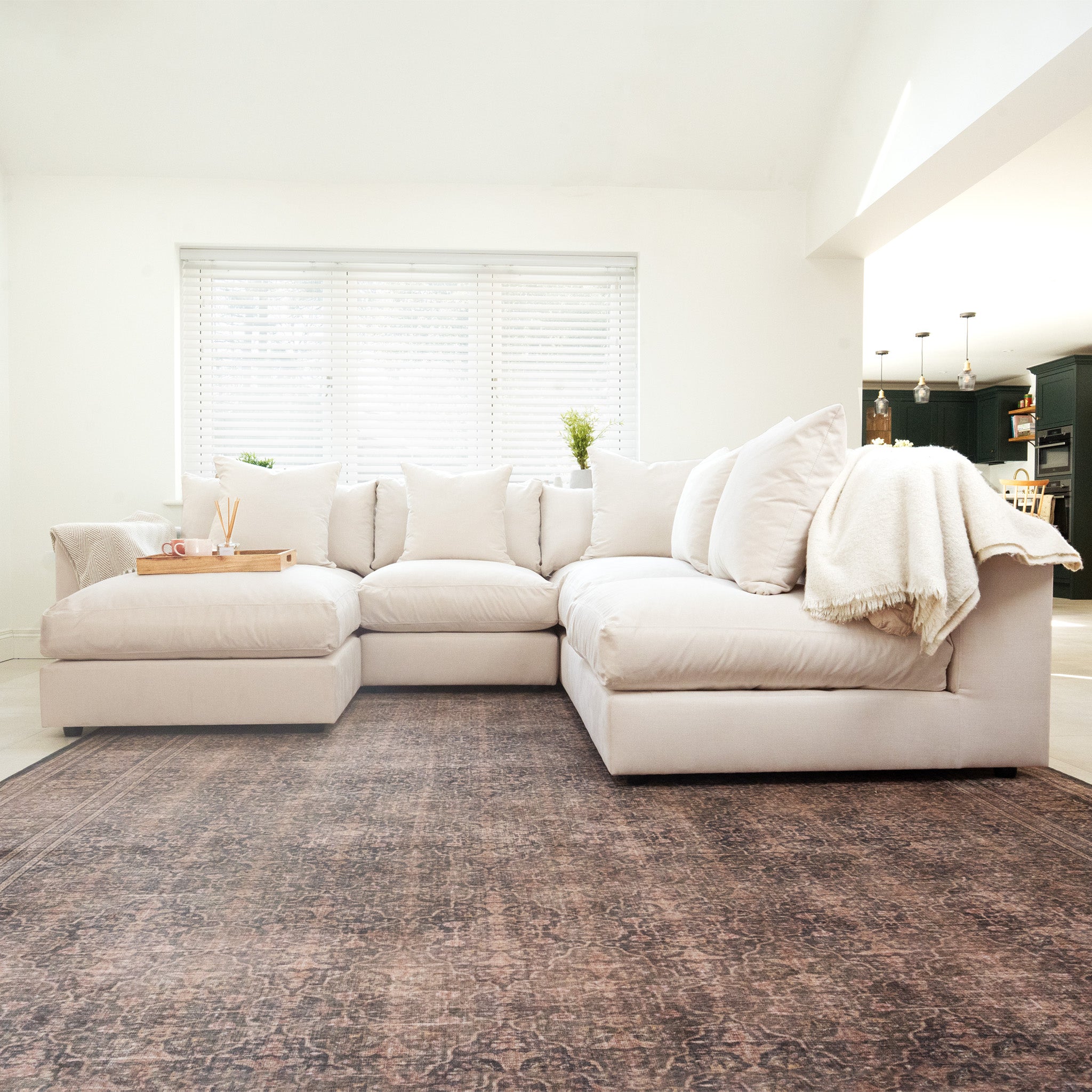 The Hampshire Modular Corner Sofa in Ivory features plush duck feather and down cushions, styled with a throw blanket in a bright living room atop a patterned rug.