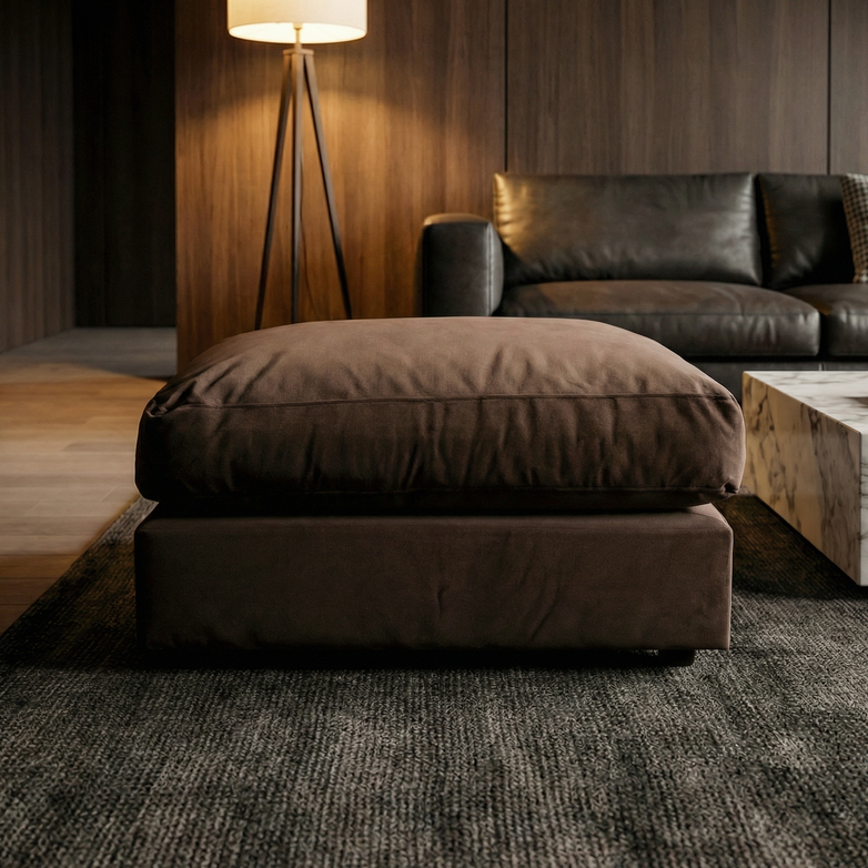 The Hampshire Modular Footstool in Cocoa features linen-effect fabric and is handmade in England, shown here on a rug in a modern living room with a leather sofa, lamp, and marble coffee table for timeless style.