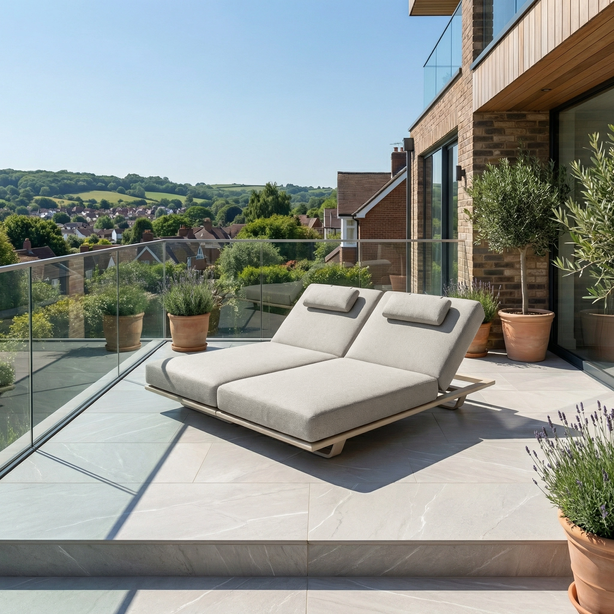 The Hatia Double Sun Lounger in Latte, featuring plush Olefin cushions, sits on a sunny balcony amid potted plants and scenic rooftop and greenery views.