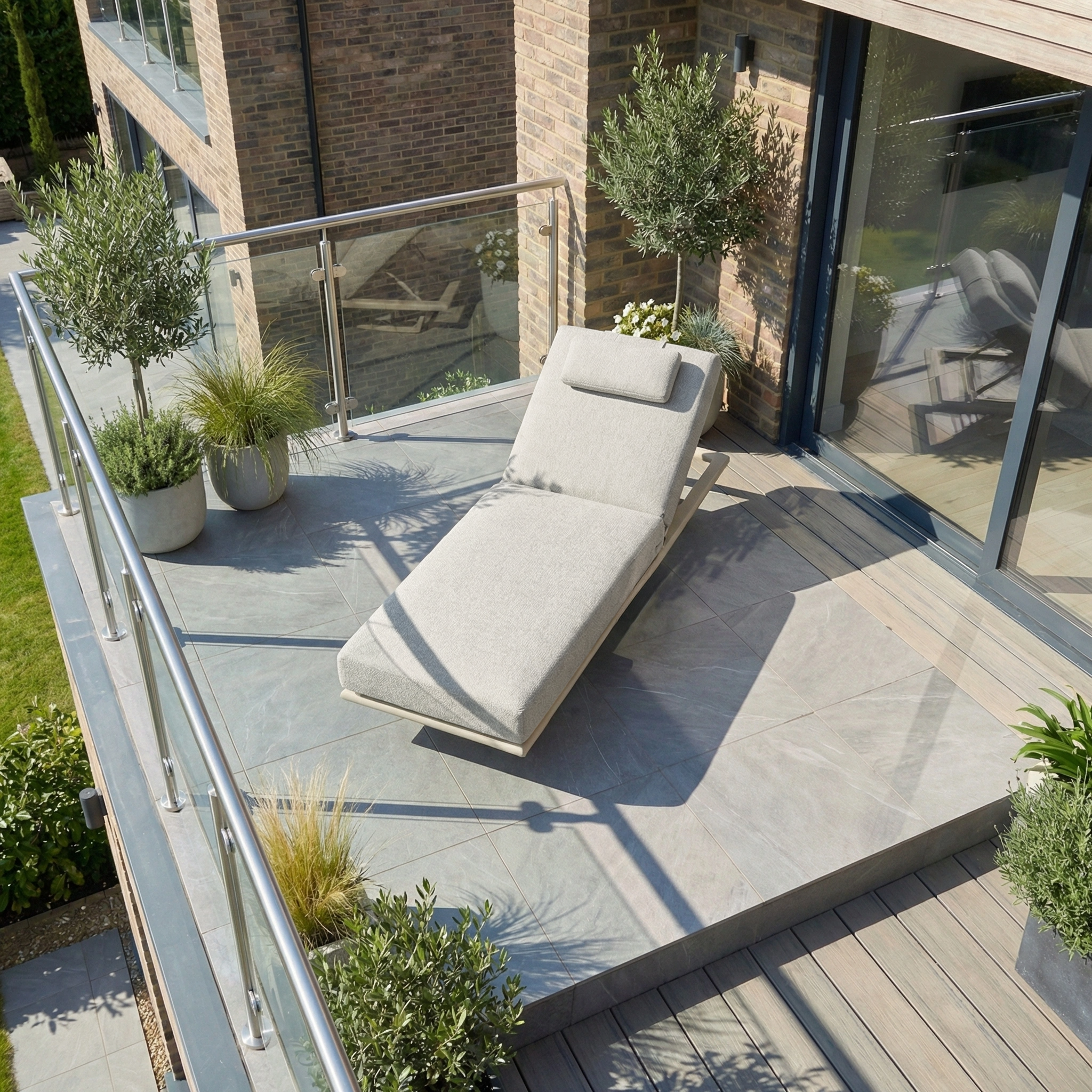 The Hatia Single Sun Lounger in Latte sits on a modern balcony with potted plants and a glass railing, offering a perfect spot for outdoor relaxation.